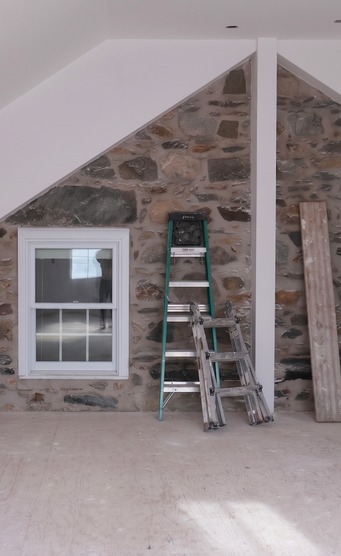 Chantier de rénovation intérieure par Studio Lagom, mettant en valeur la préservation d'un mur de pierre naturelle sous un plafond mansardé.