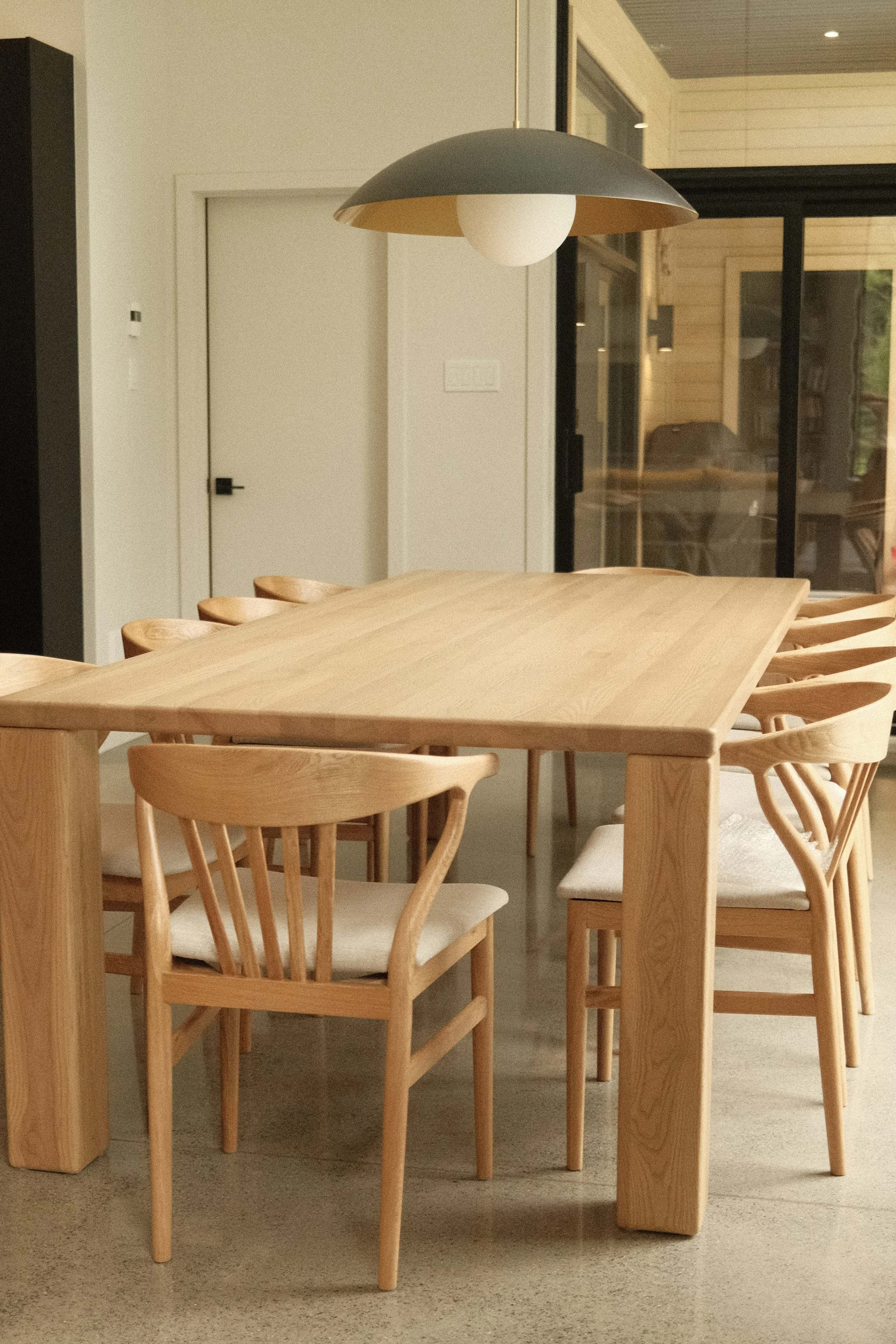 Table de salle à manger en bois clair massif et ses chaises scandinaves design, surmontée d'un luminaire moderne, par Studio Lagom.