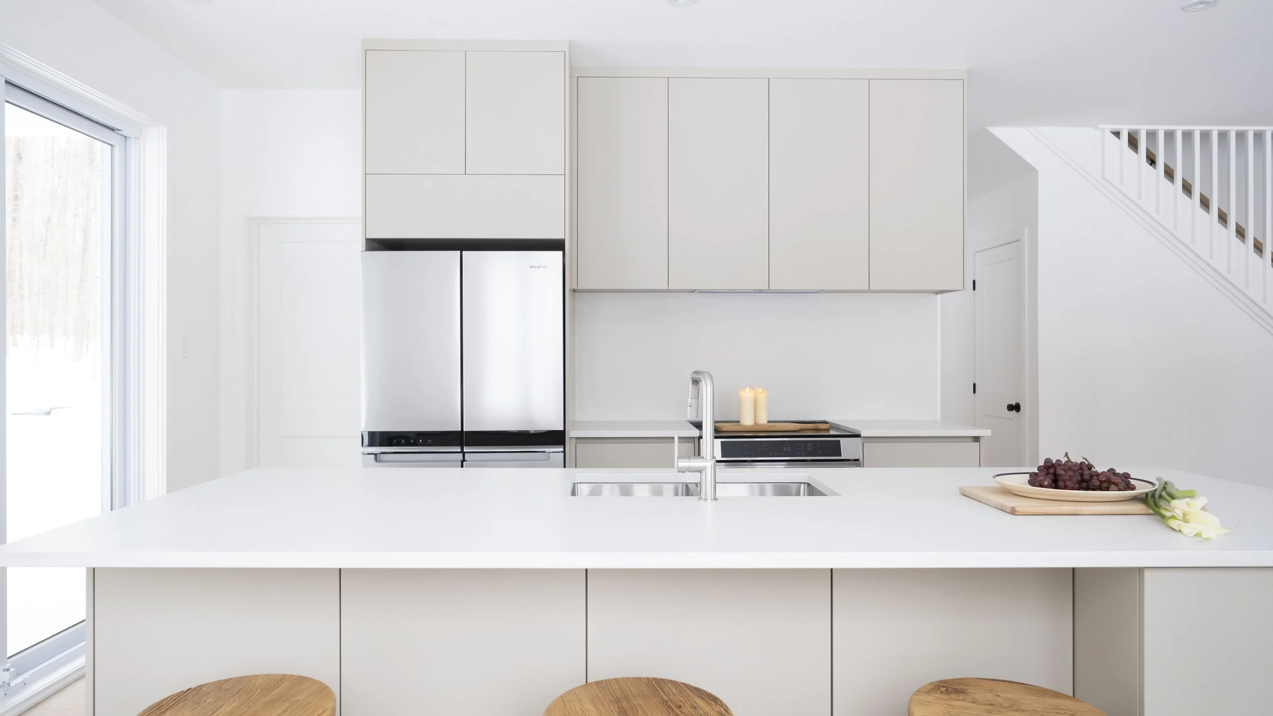 Design d'intérieur d'une cuisine moderne et lumineuse avec armoires sur mesure aux tons neutres et îlot central blanc, une réalisation de Studio Lagom.