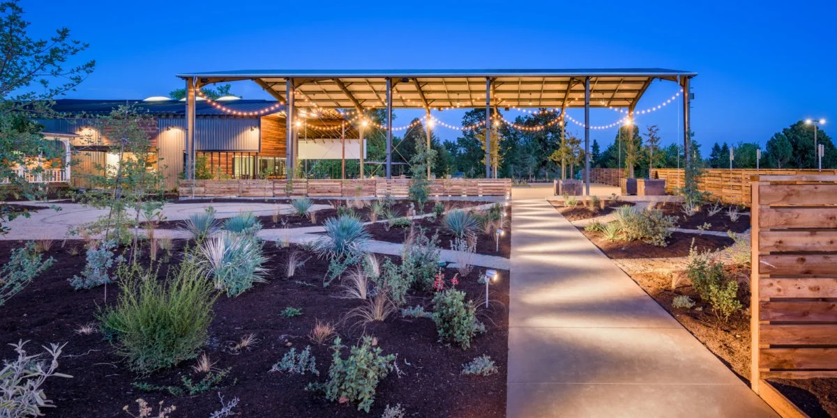 Outdoor event space with string lights, a covered pavilion, and a landscaped garden with drought-tolerant plants, in the evening.