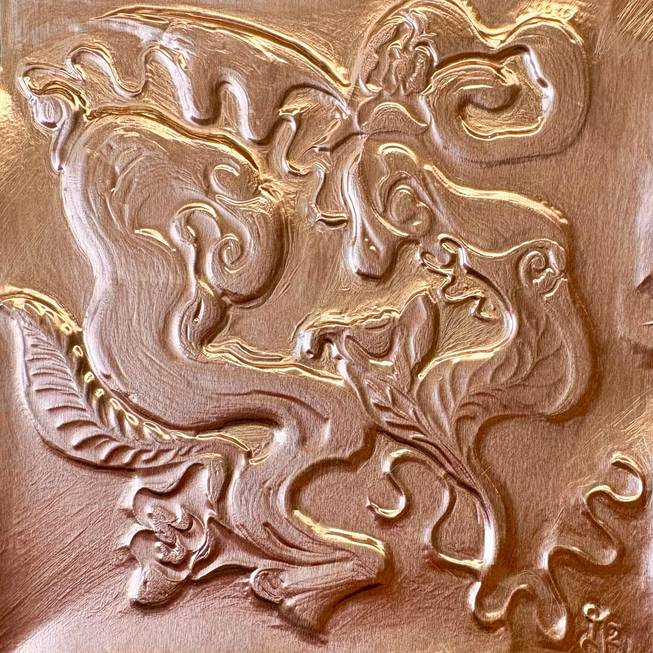 Close-up of an embossed metallic artwork featuring a face surrounded by swirling, flowing lines and decorative details.