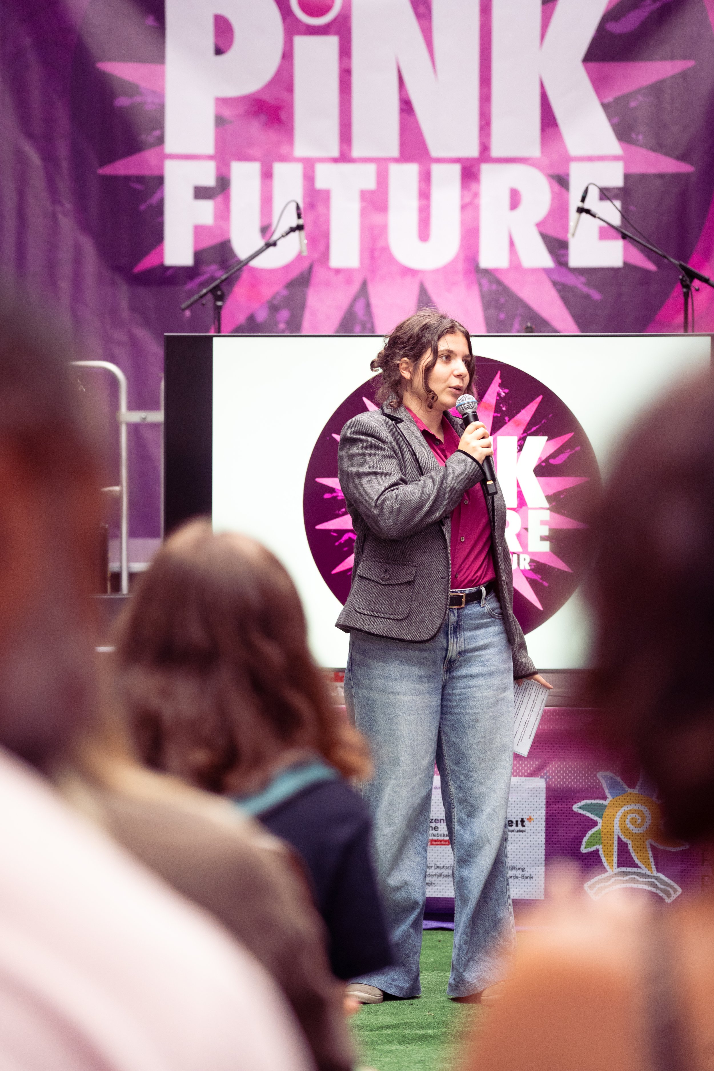 Frau spricht bei einer Veranstaltung mit Pink-Future-Logo im Hintergrund.