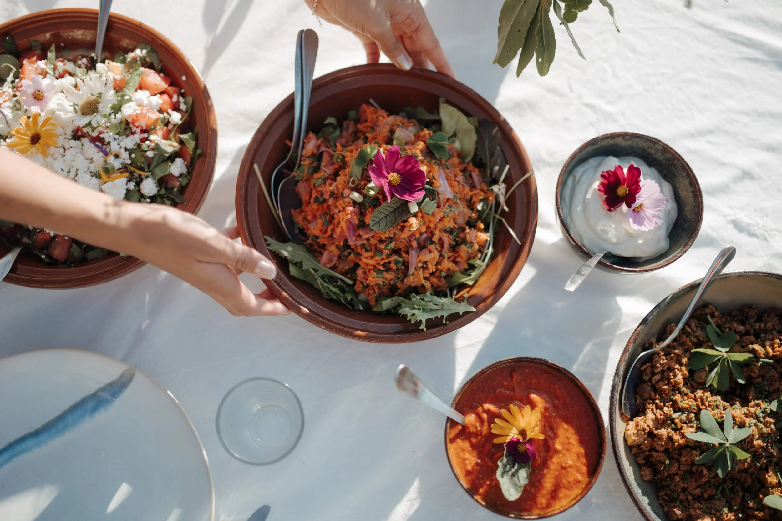 Various bowls of colorful salads and dips decorated with edible flowers on a white surface.
