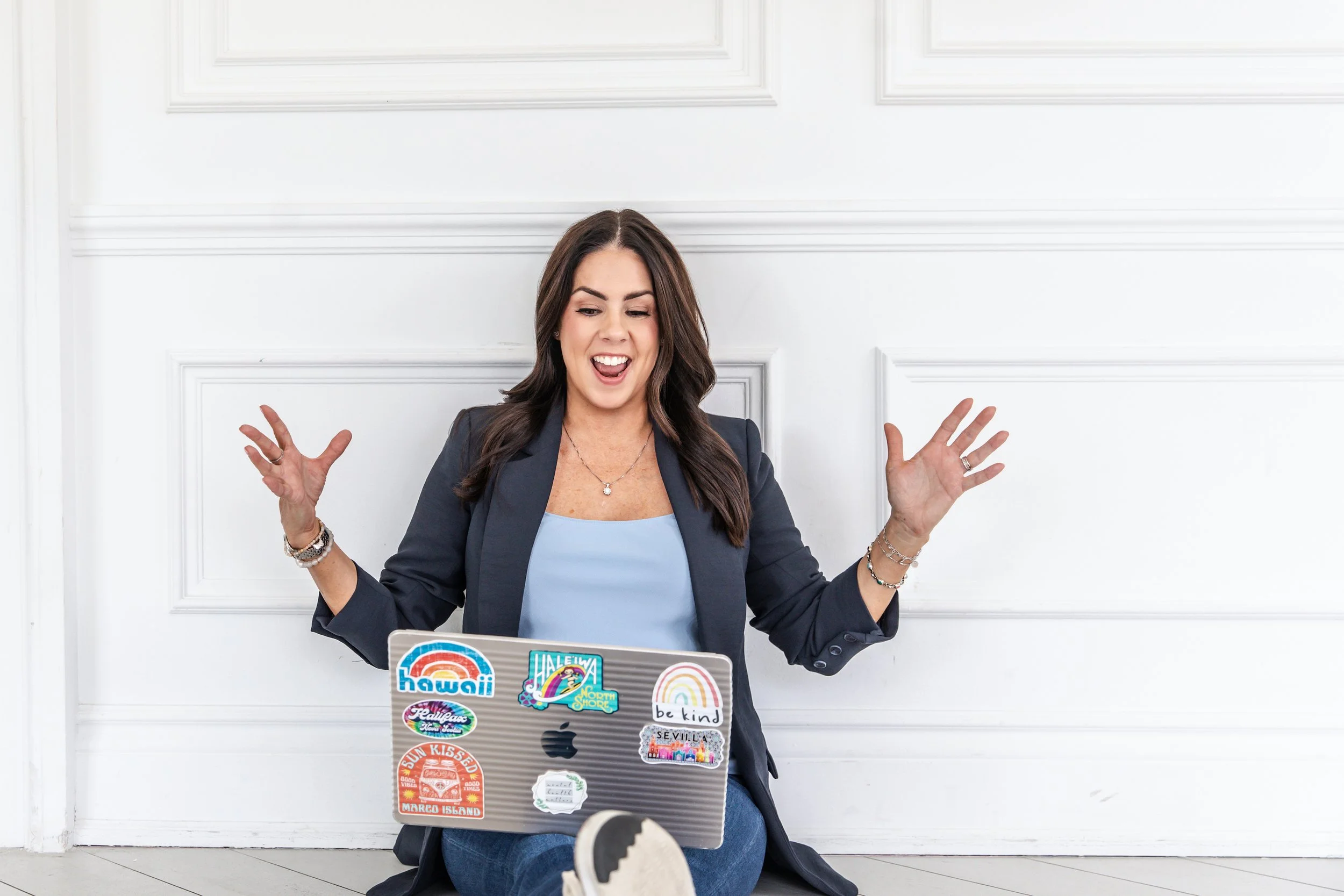 Danielle Pomeroy, SHSM Ontario certification provider, smiles joyfully holding a sticker-covered laptop on a white paneled wall. 