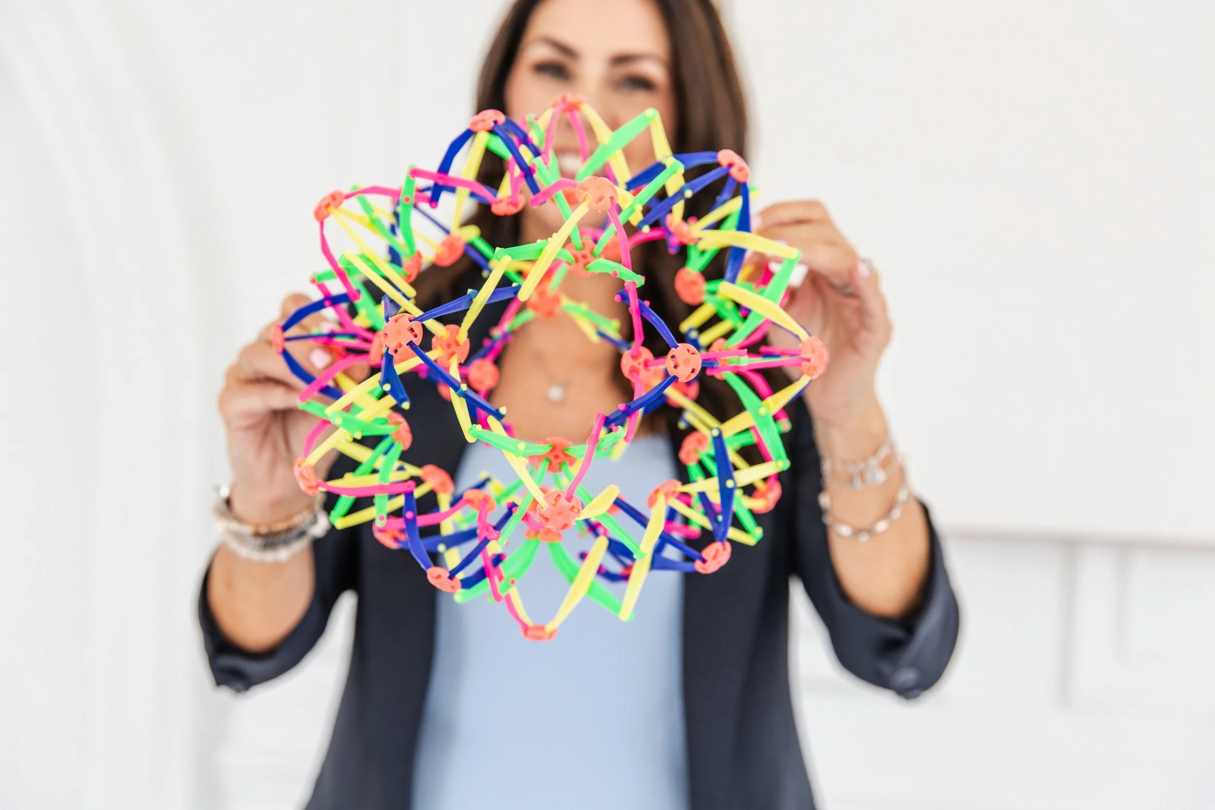 A smiling woman in a blazer, mental health guest speaker in GTA Danielle Pomeroy, displays a bright Zolo fidget toy structure.