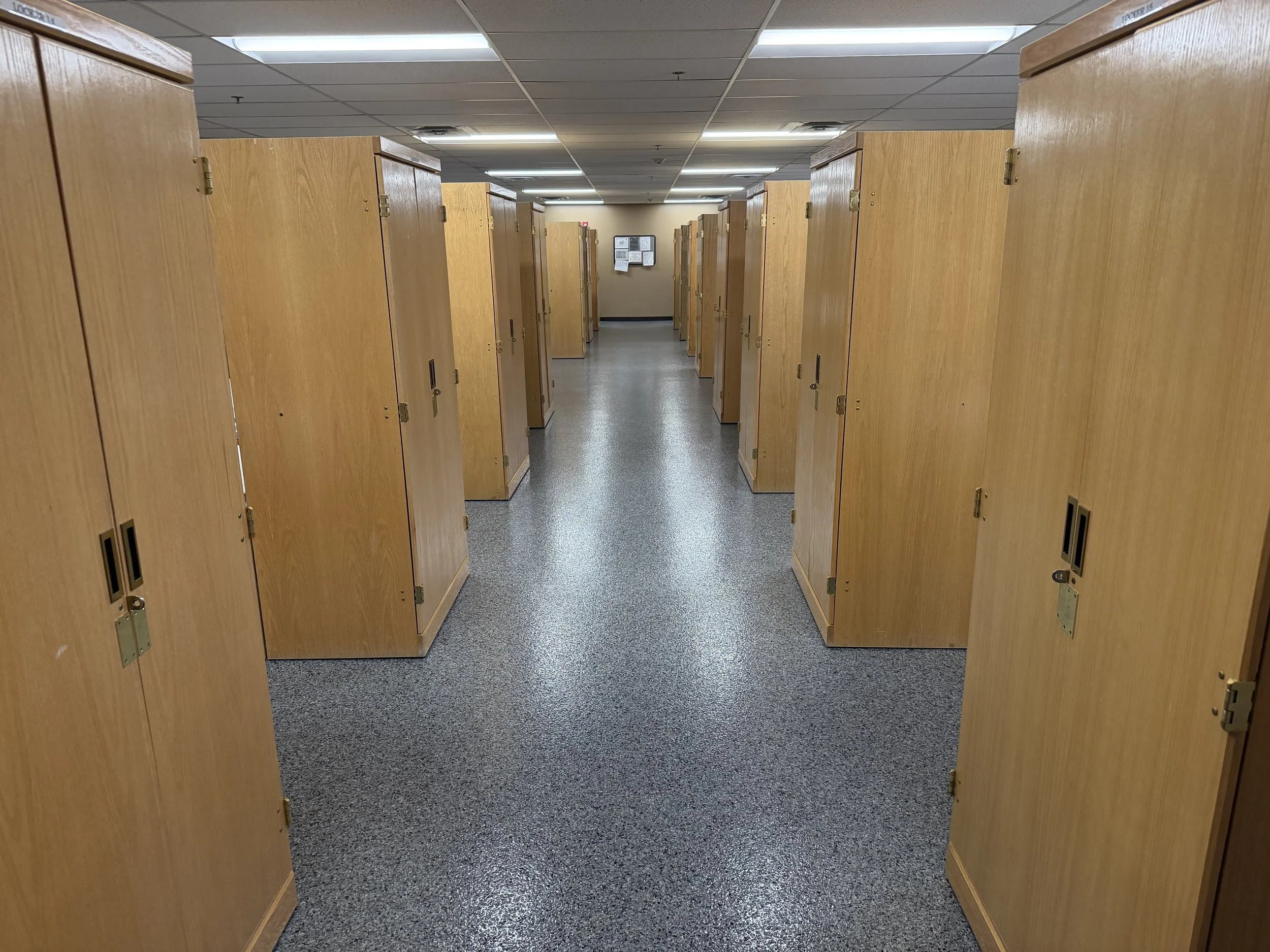 Empty open-bay hallway with wooden lockers on both sides and bulletin boards at the end.
