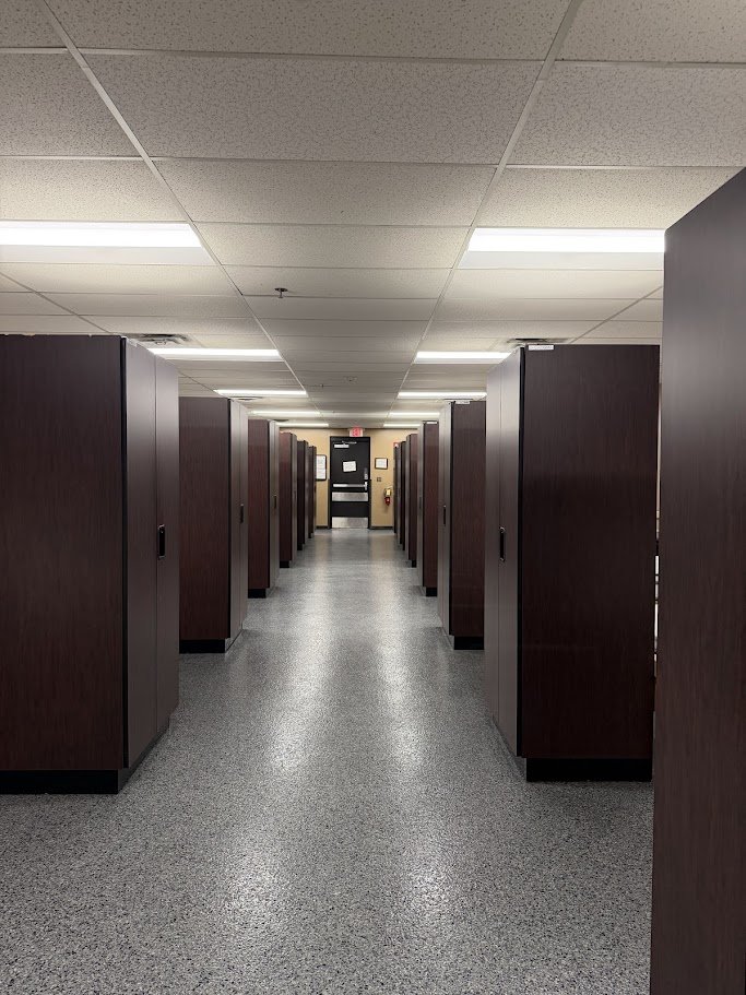 Empty hallway in a building with dark wooden lockers and a black door at the end.