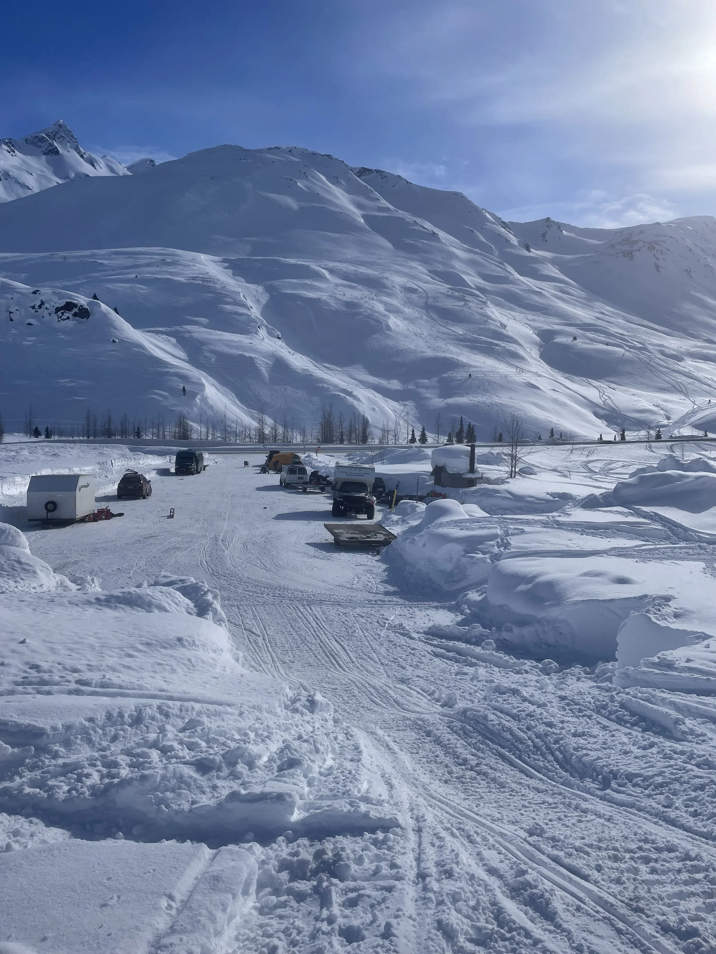 Snow-covered mountain landscape with parked vehicles and ski tracks on the snow.
