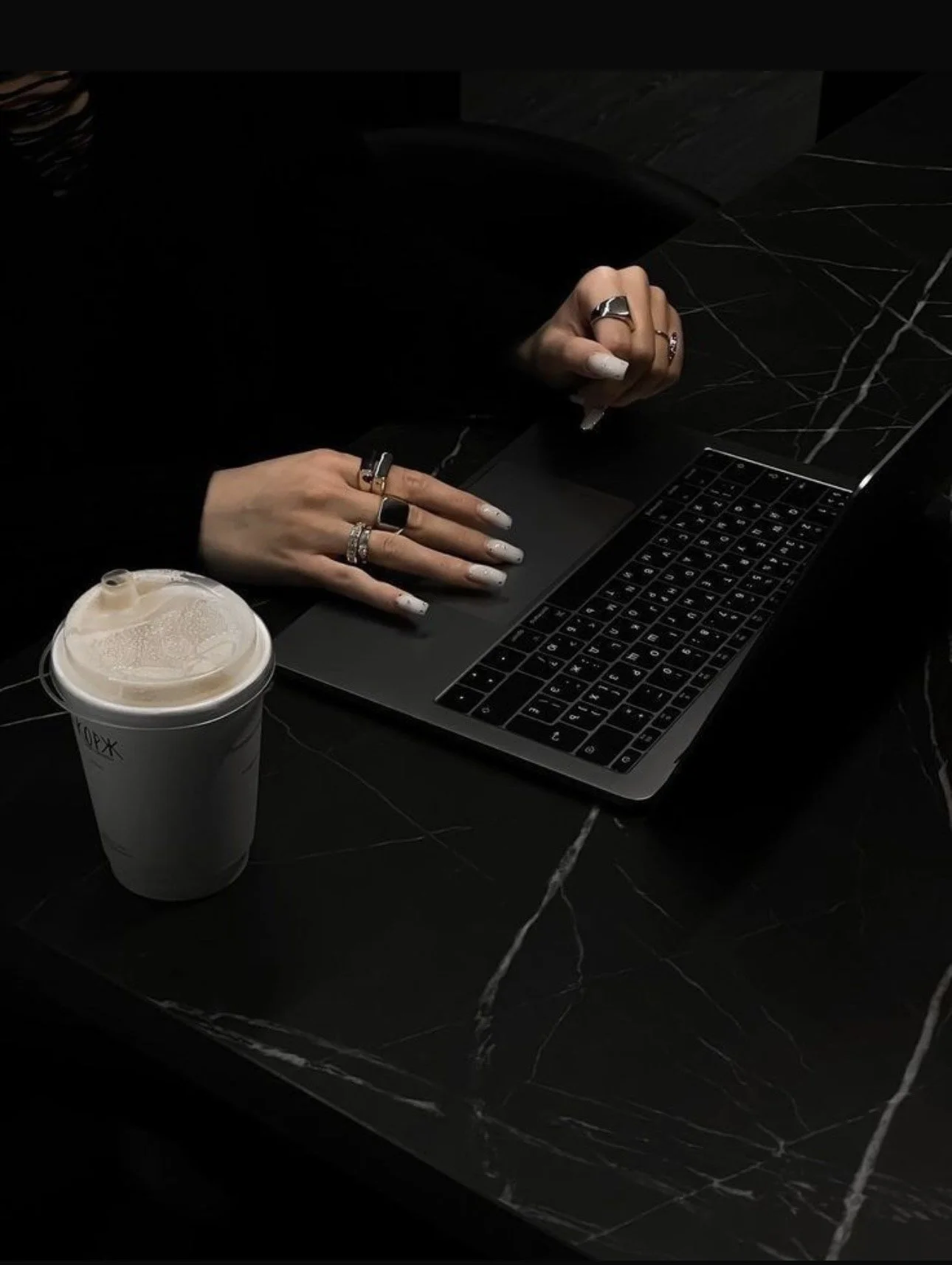 Person using a laptop on a black marble table with a disposable coffee cup nearby.