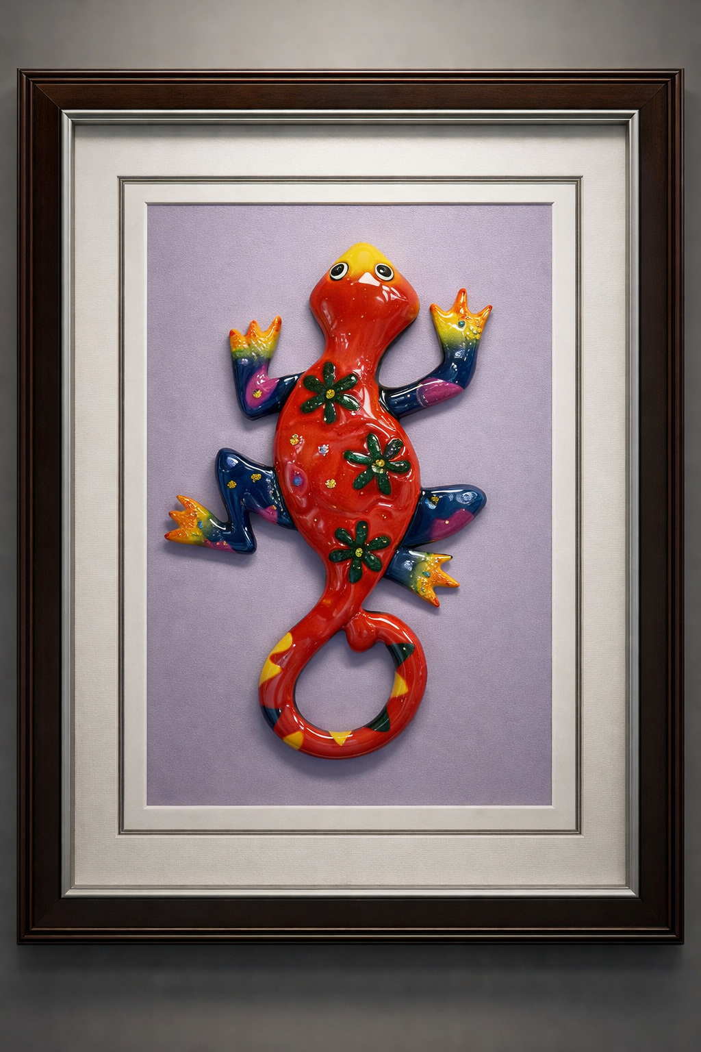 Colorful ceramic lizard wall art with green flower patterns on its body, mounted on a purple background within a frame.