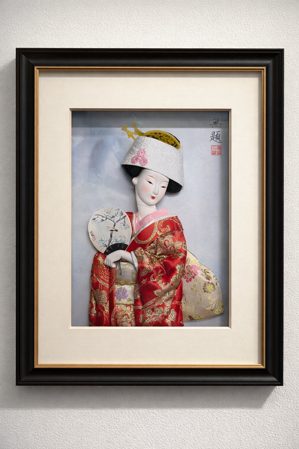 Framed artwork of a traditional Japanese doll wearing a red kimono and holding a fan, with a white hat and stylized background.