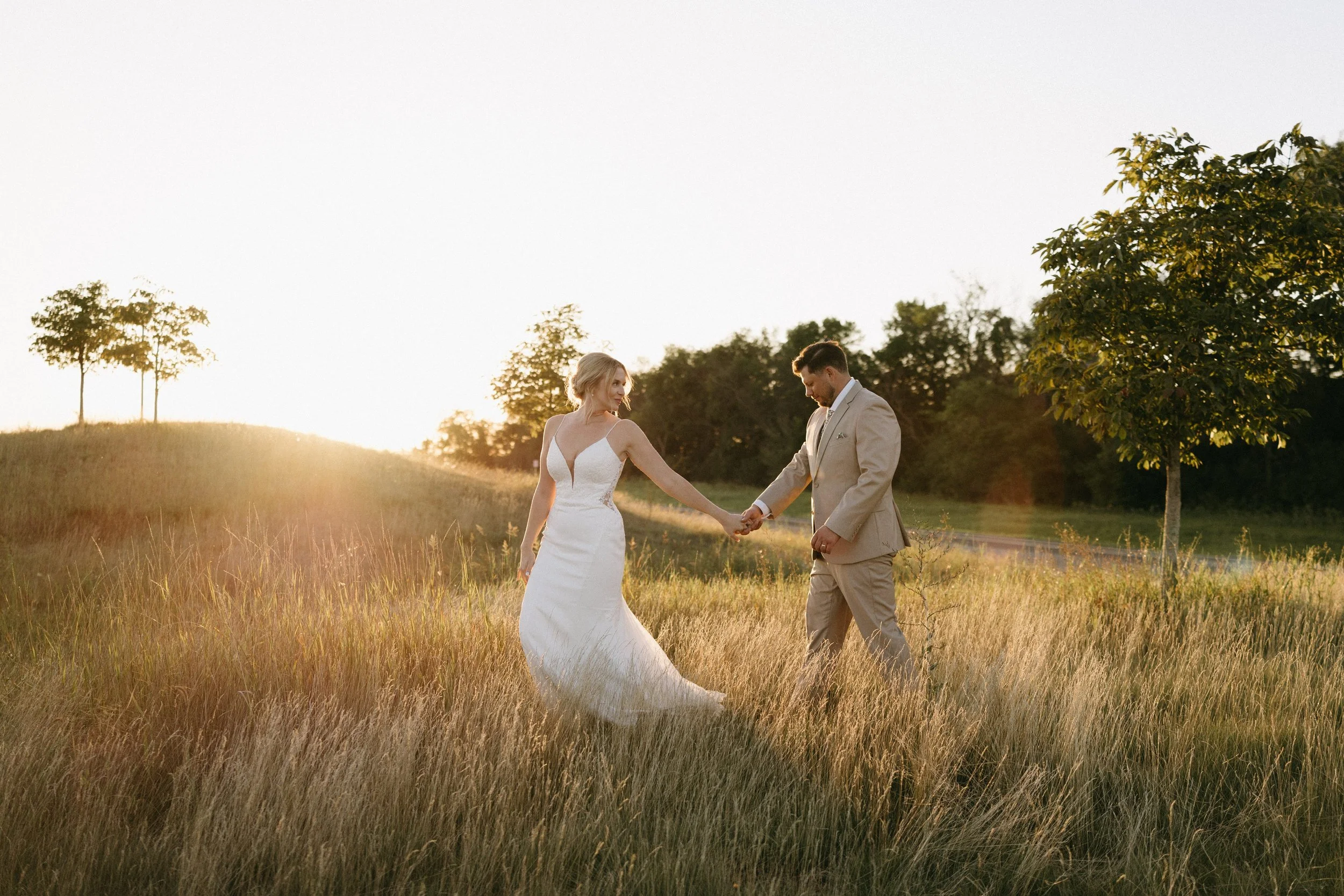 A bride and groom holding hands in a field at sunset.