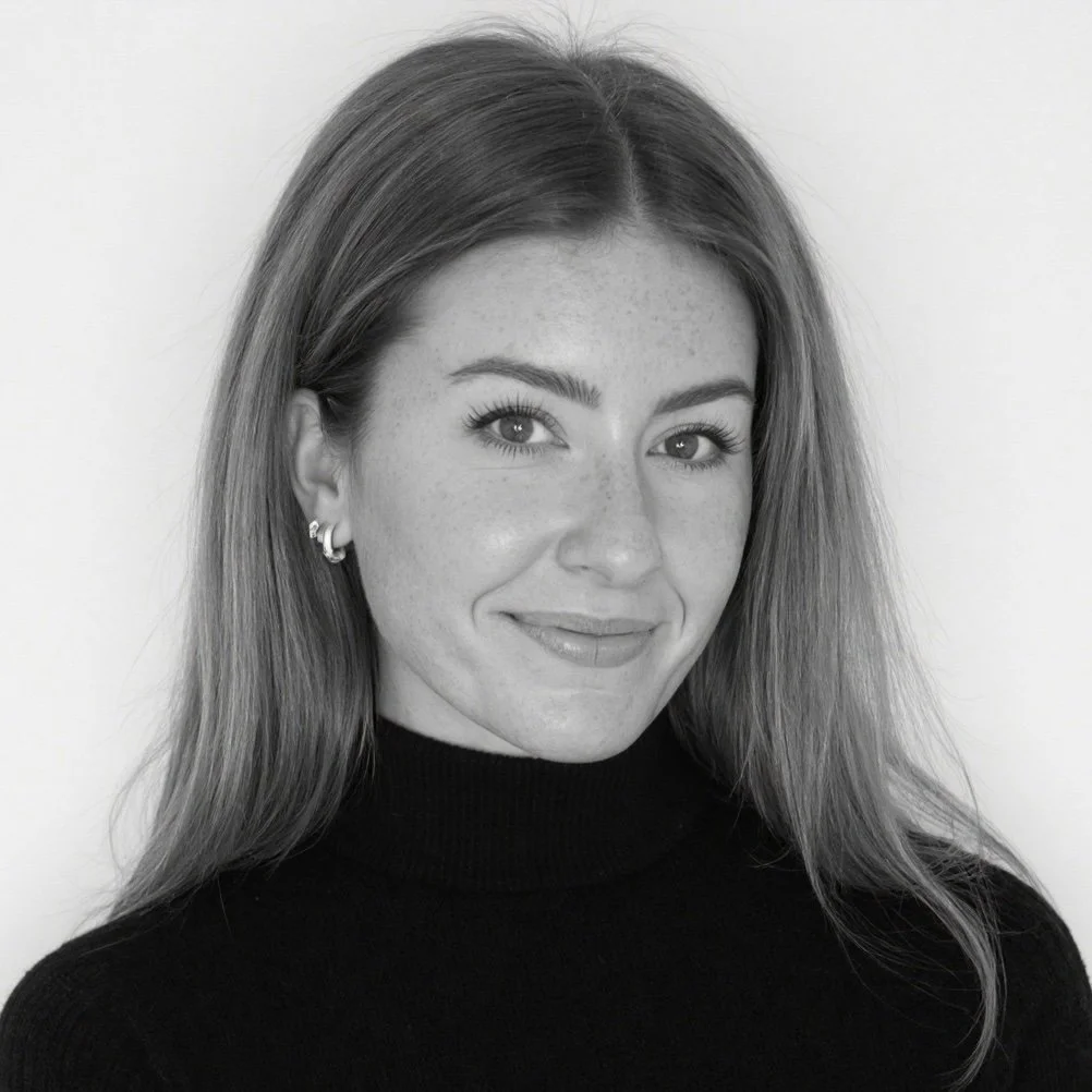 Headshot of a young woman with long hair, wearing a black turtleneck, smiling, against a plain background.