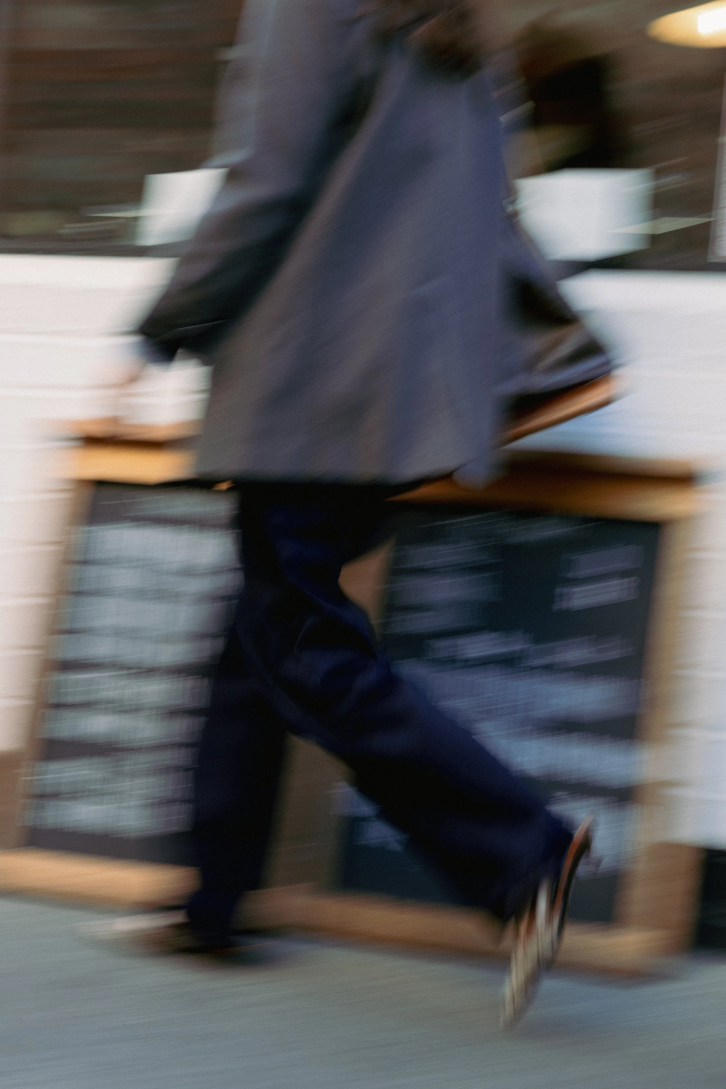 A person walking past a chalkboard menu outside a café or restaurant, with motion blur.