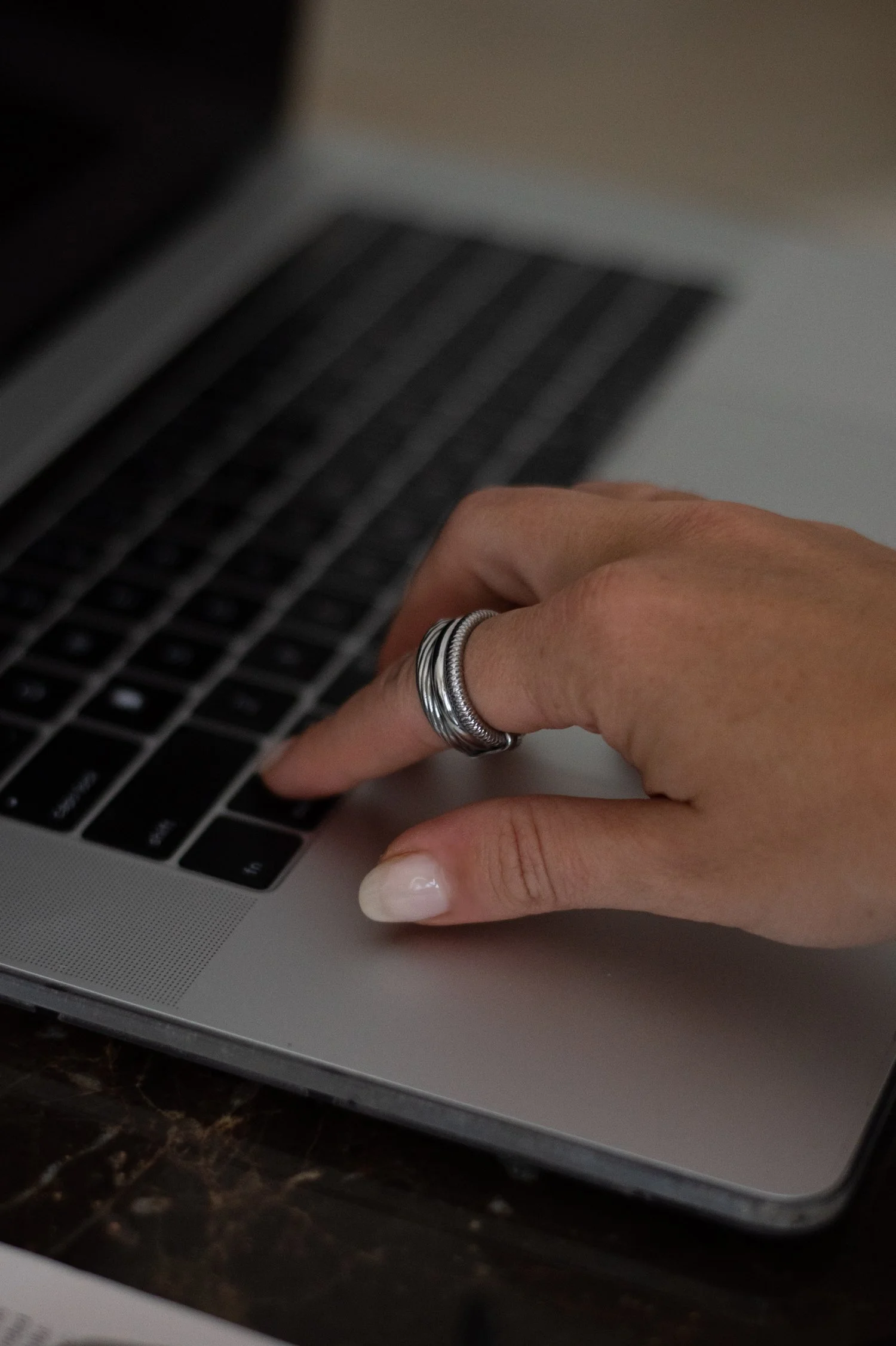 Close-up of a person's hand with silver rings, typing on a laptop keyboard.