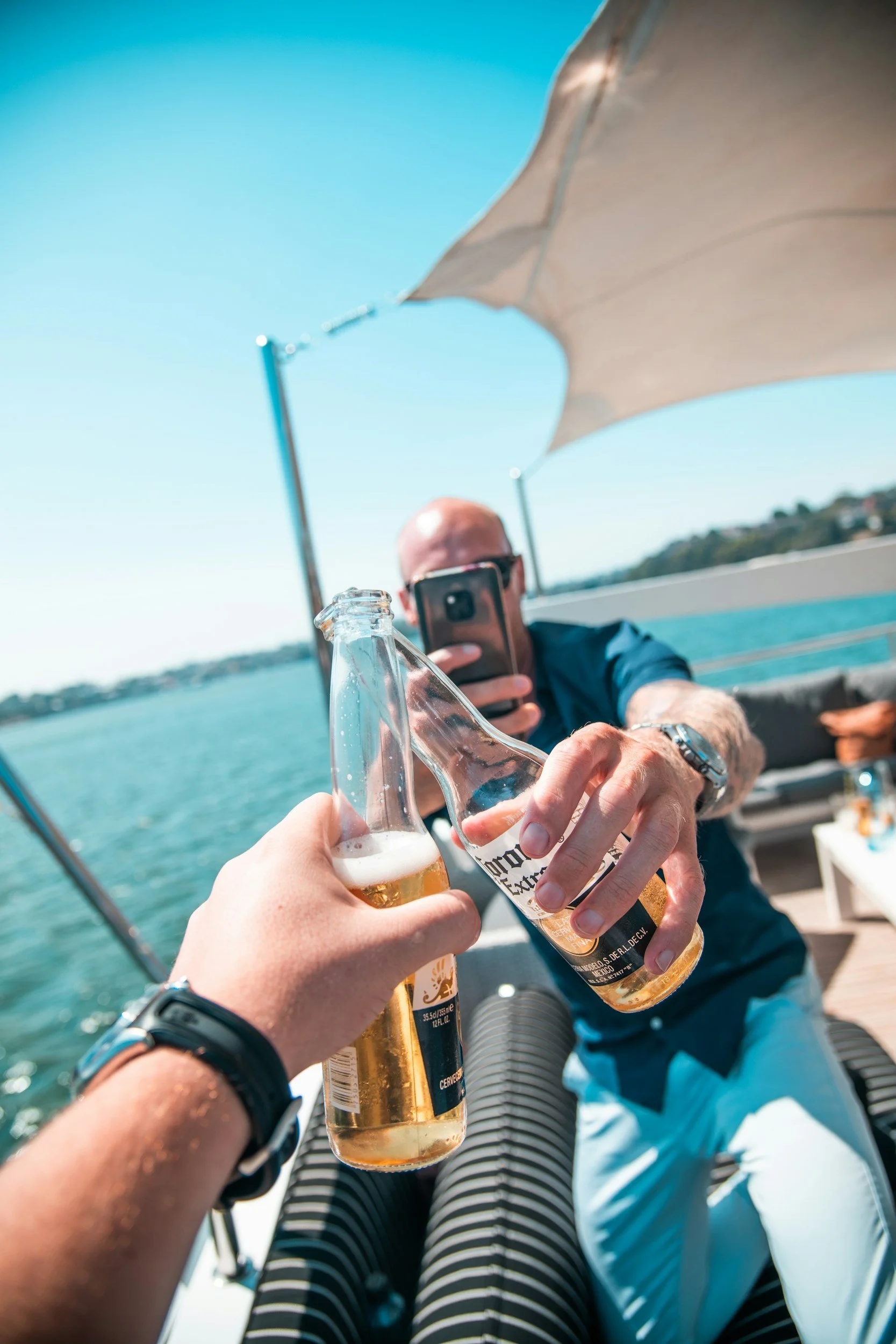 People on a boat toasting with Corona beer bottles with a water and sky background.