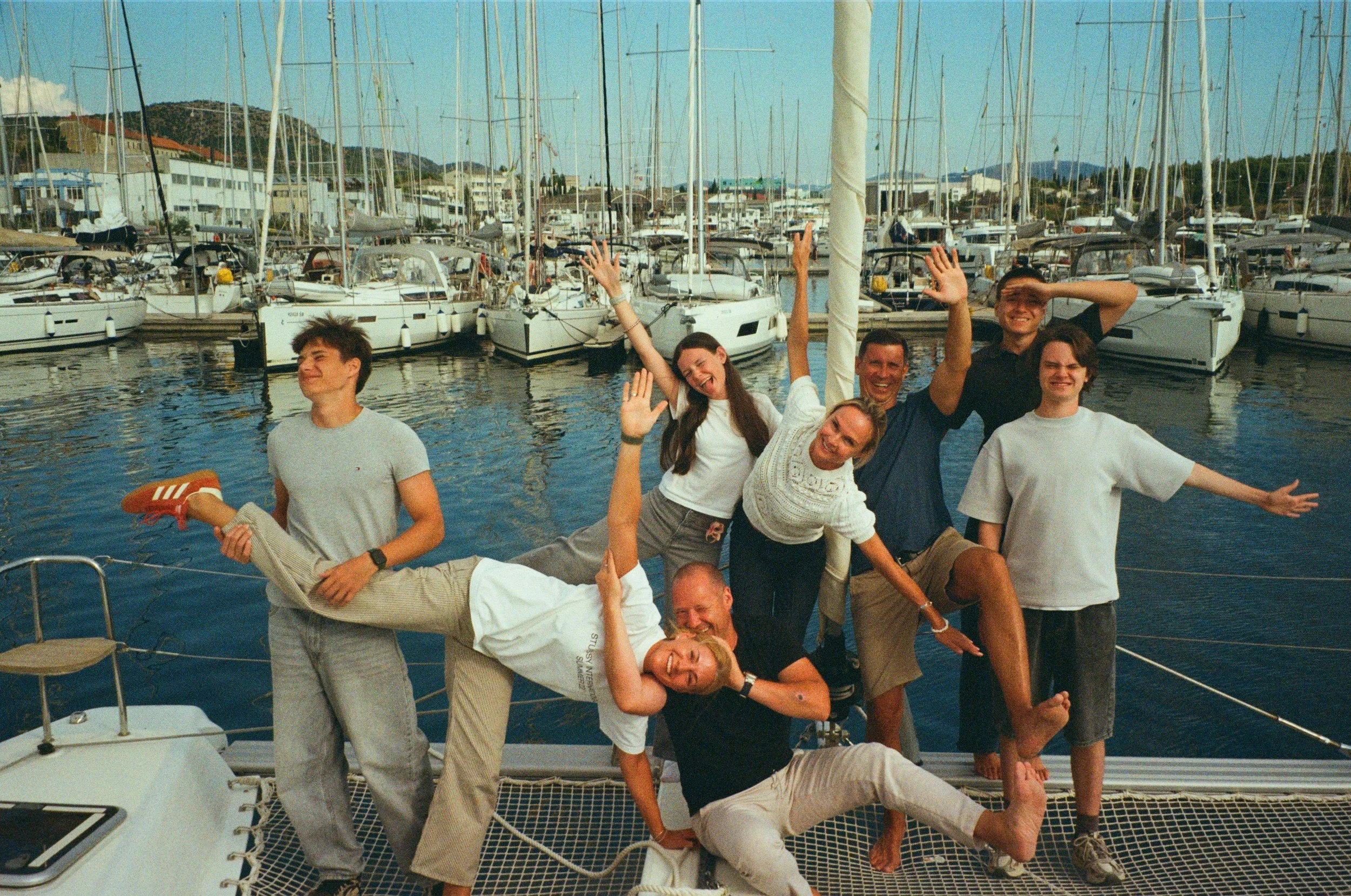 Group of people enjoying themselves on a boat at a marina with sailboats and yachts in the background.