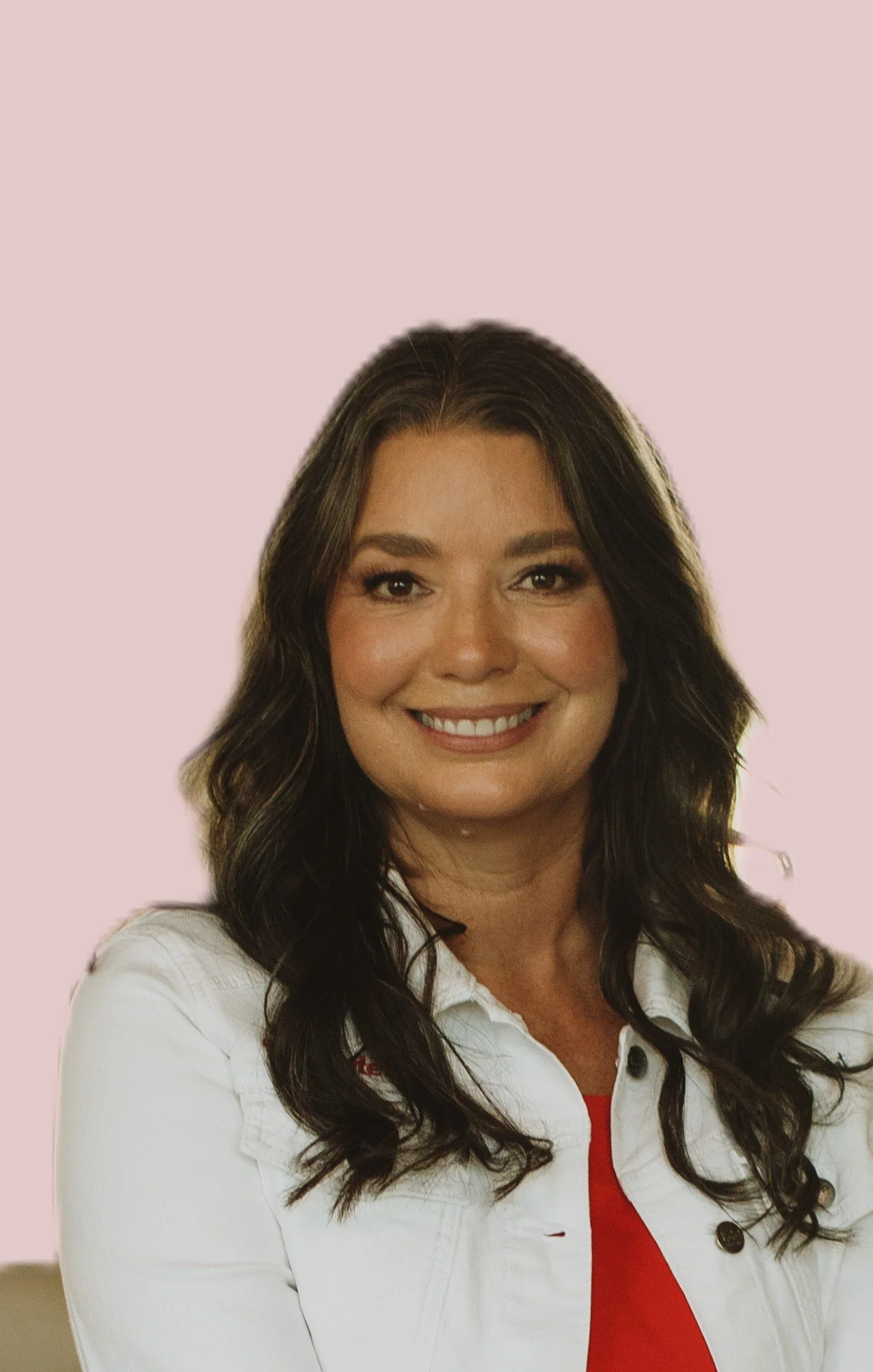 A woman with dark wavy hair, smiling, wearing a white jacket over a red top, against a light pink background.