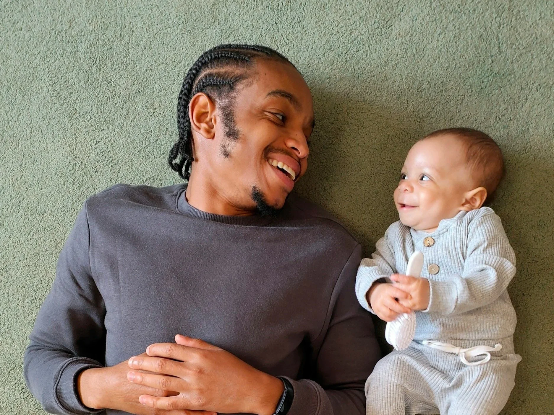 A man and a baby lying on a green carpet, facing each other and smiling representing Family Law.