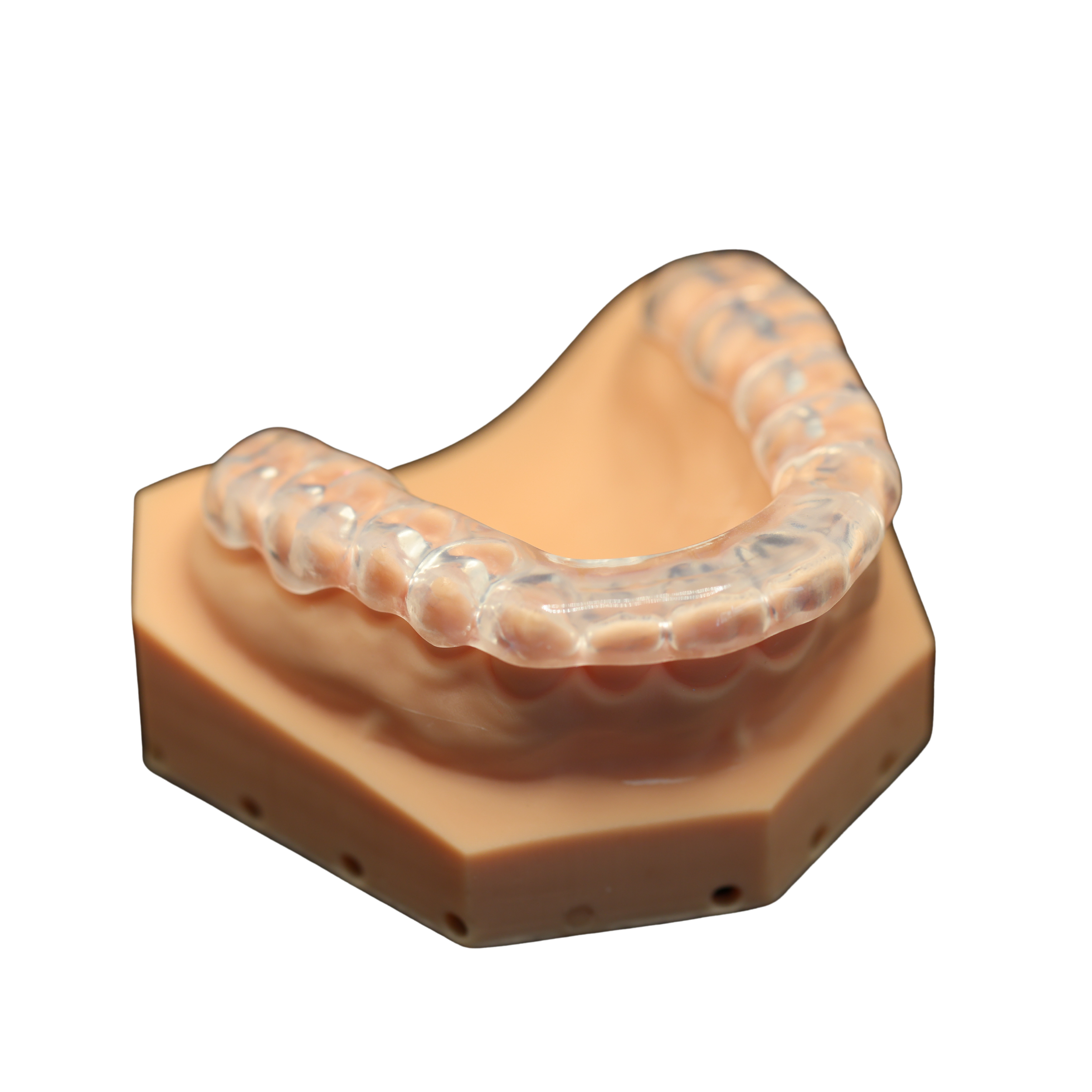 A dental model displaying a transparent clear aligner placed on a peach-colored base.