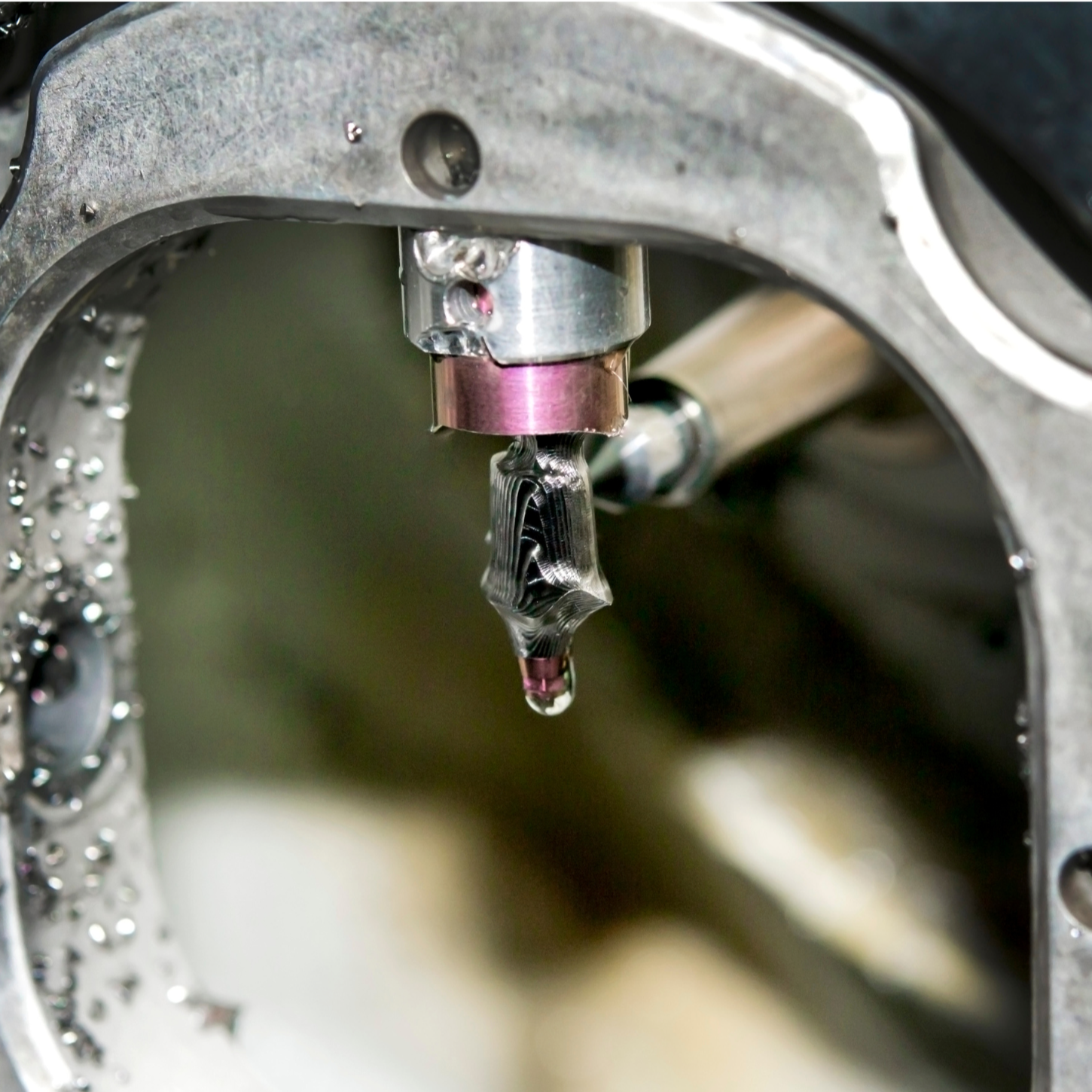 Close-up of a machine part with a metal drill bit and a drop of liquid at the tip.