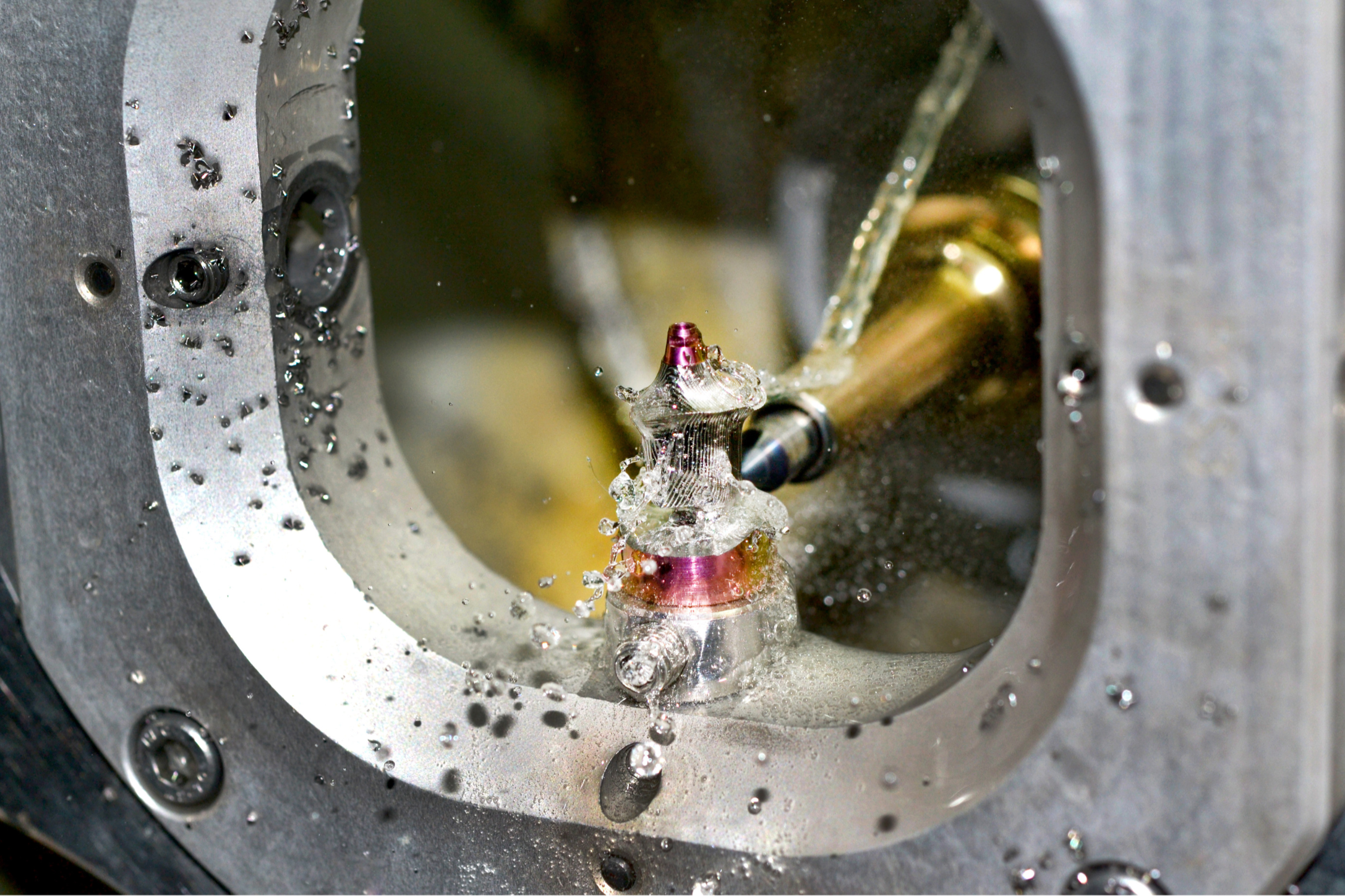 Close-up of a high-precision machining process with water coolant spraying onto a metal component, possibly in an industrial manufacturing setting.