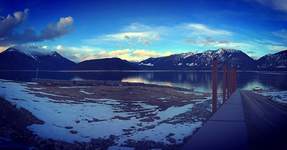 Scenic view of a lake surrounded by snow-capped mountains during sunset with a dock extending into the water.