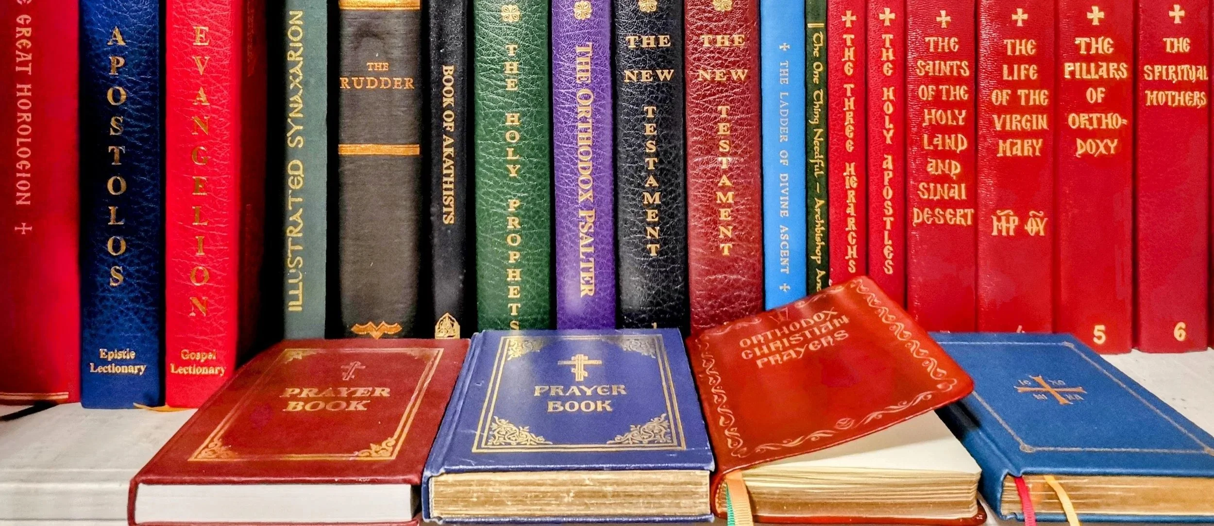 Shelf of religious books, including prayer books and Bible, with colorful covers and gold lettering, arranged vertically.