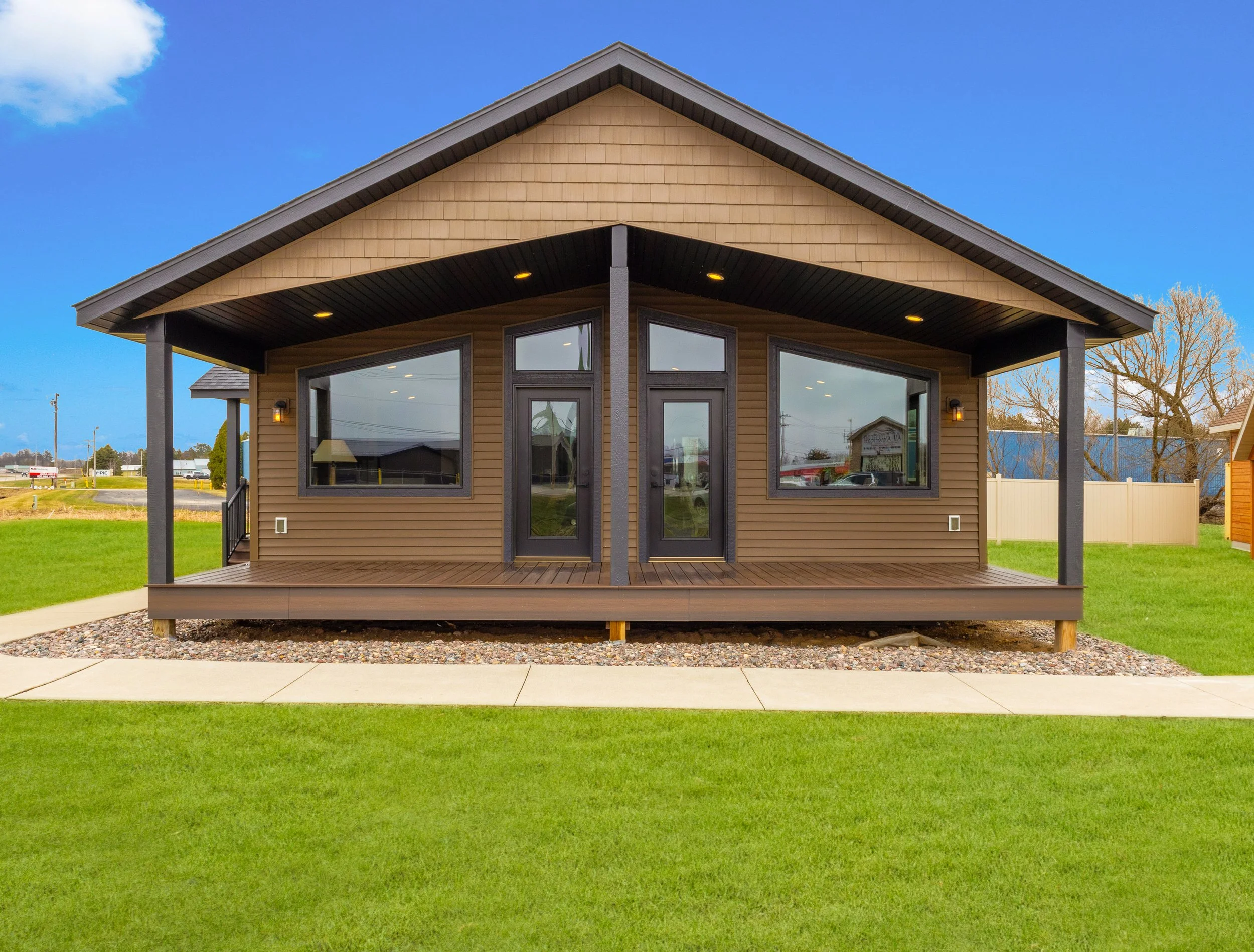 Front view of a modern house with large windows, wooden siding, a covered porch with black supports, and a well-maintained grassy yard.