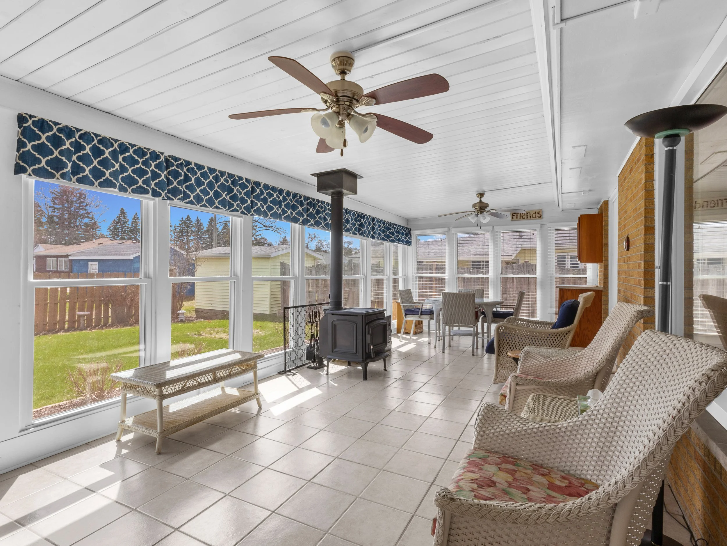 Sunroom with white ceiling, ceiling fans, large windows, patio furniture, and a pellet stove.