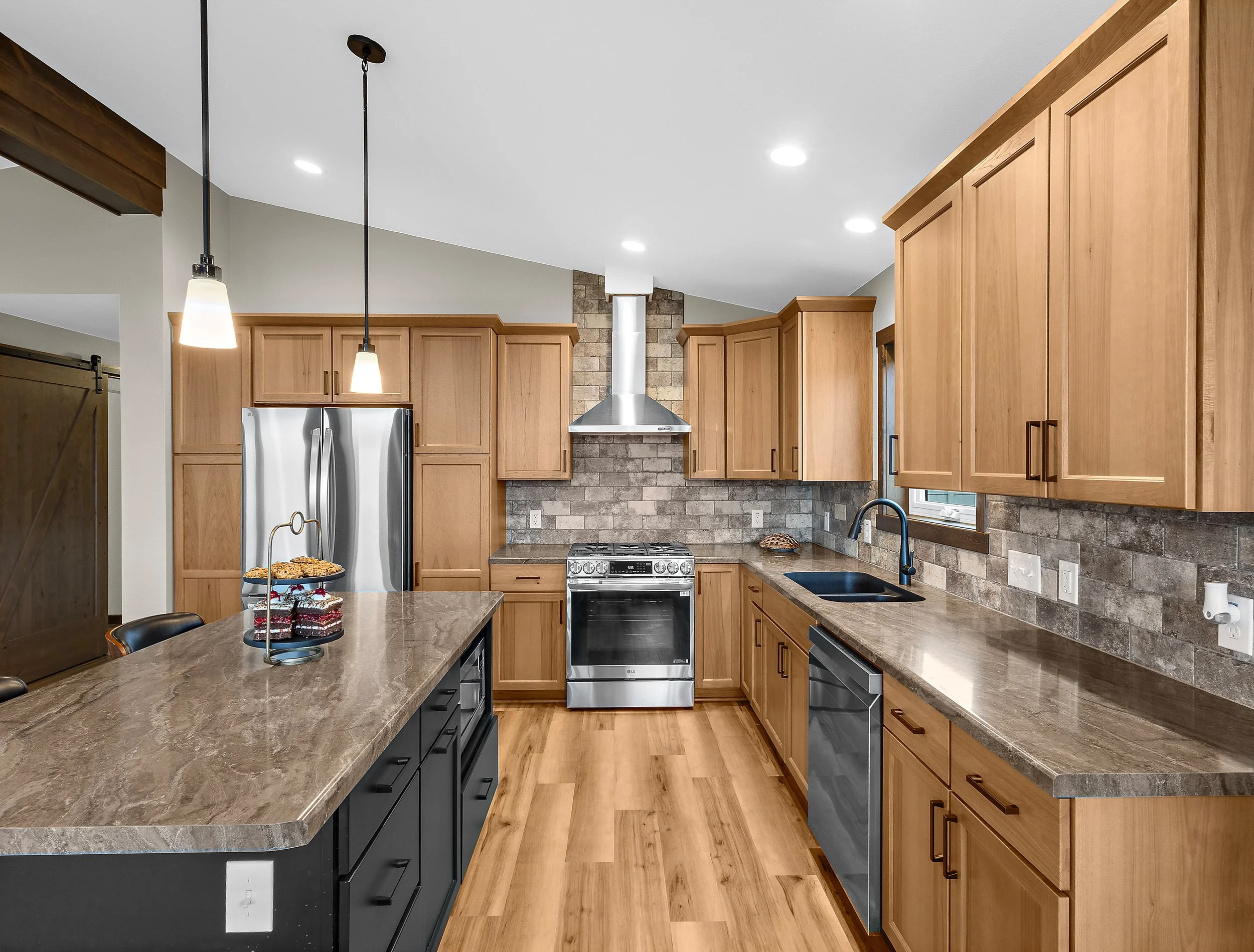 Modern kitchen with wooden cabinets, stainless steel appliances, brick backsplash, and pendant lights over a marble countertop.