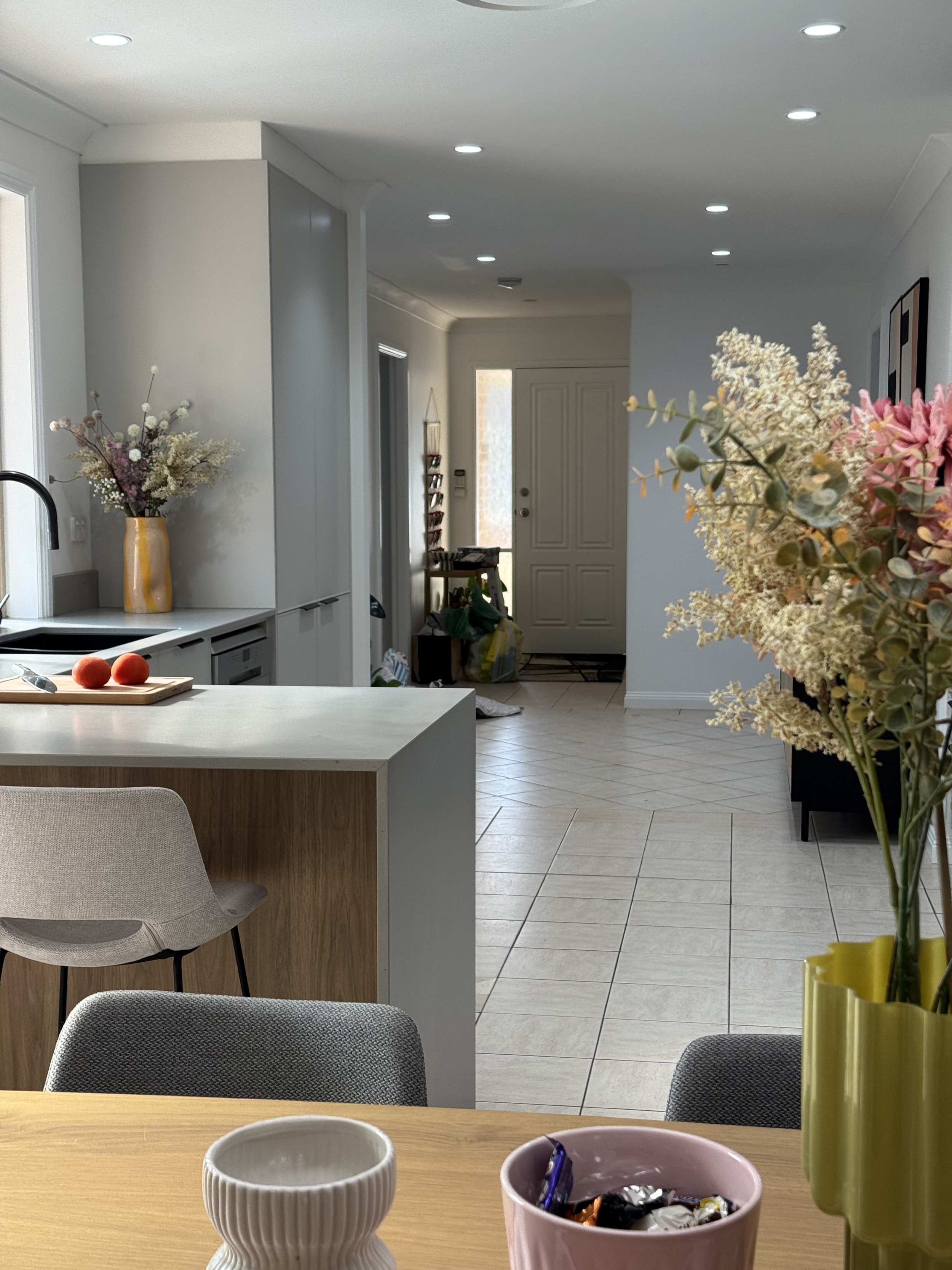 A view of a bright, modern kitchen with a white countertop, a beige chair, and decorative flowers on the table and in the background near the door.