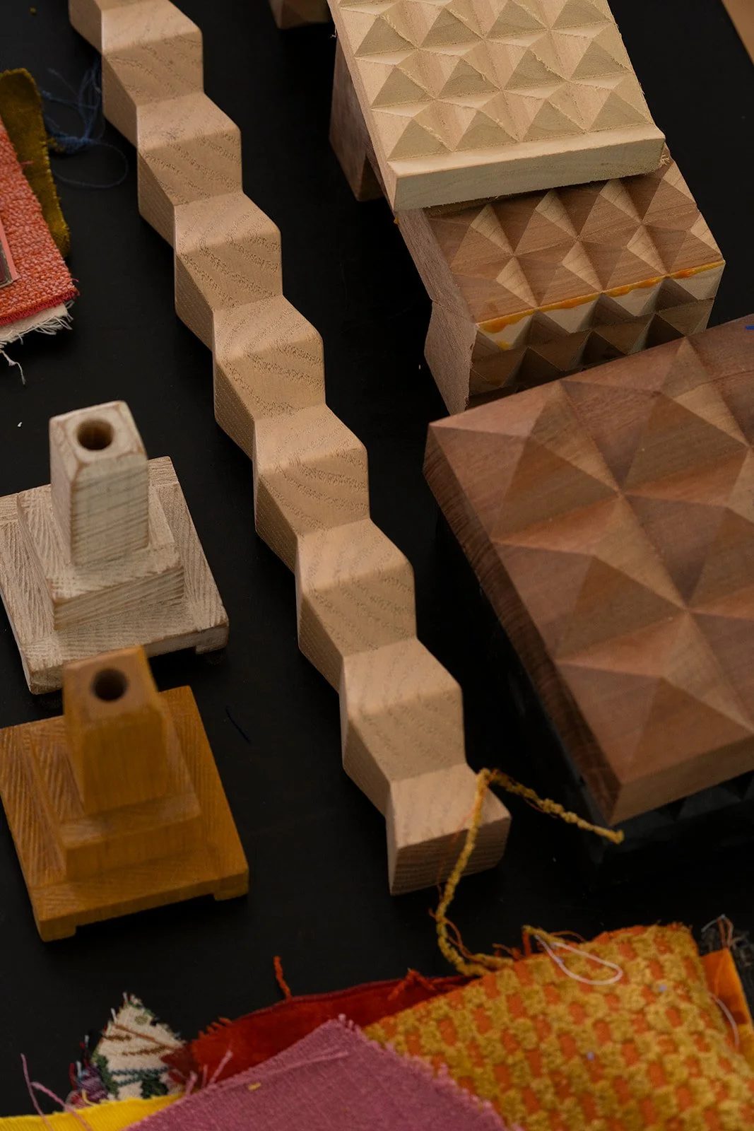 Various wooden objects with geometric patterns, including a long zigzag-shaped piece and square blocks with pyramid-like carvings, placed on a black surface.