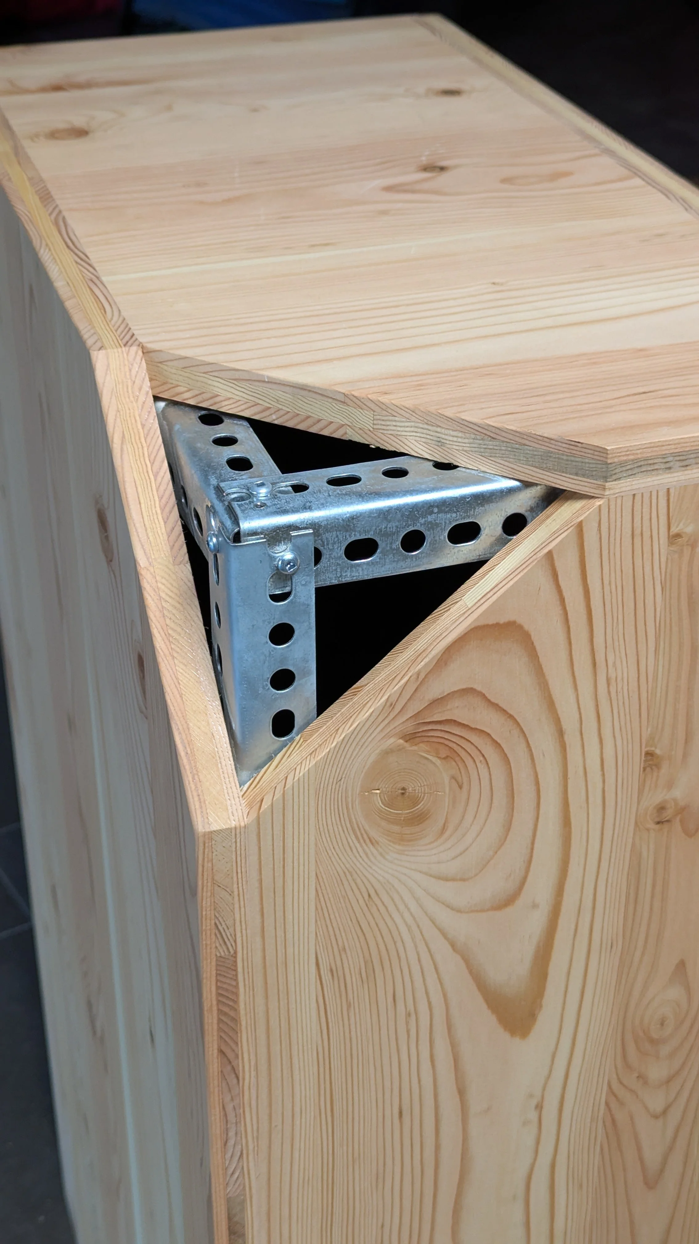 Unfinished tall wooden cabinet with an open top corner revealing metal brackets inside.