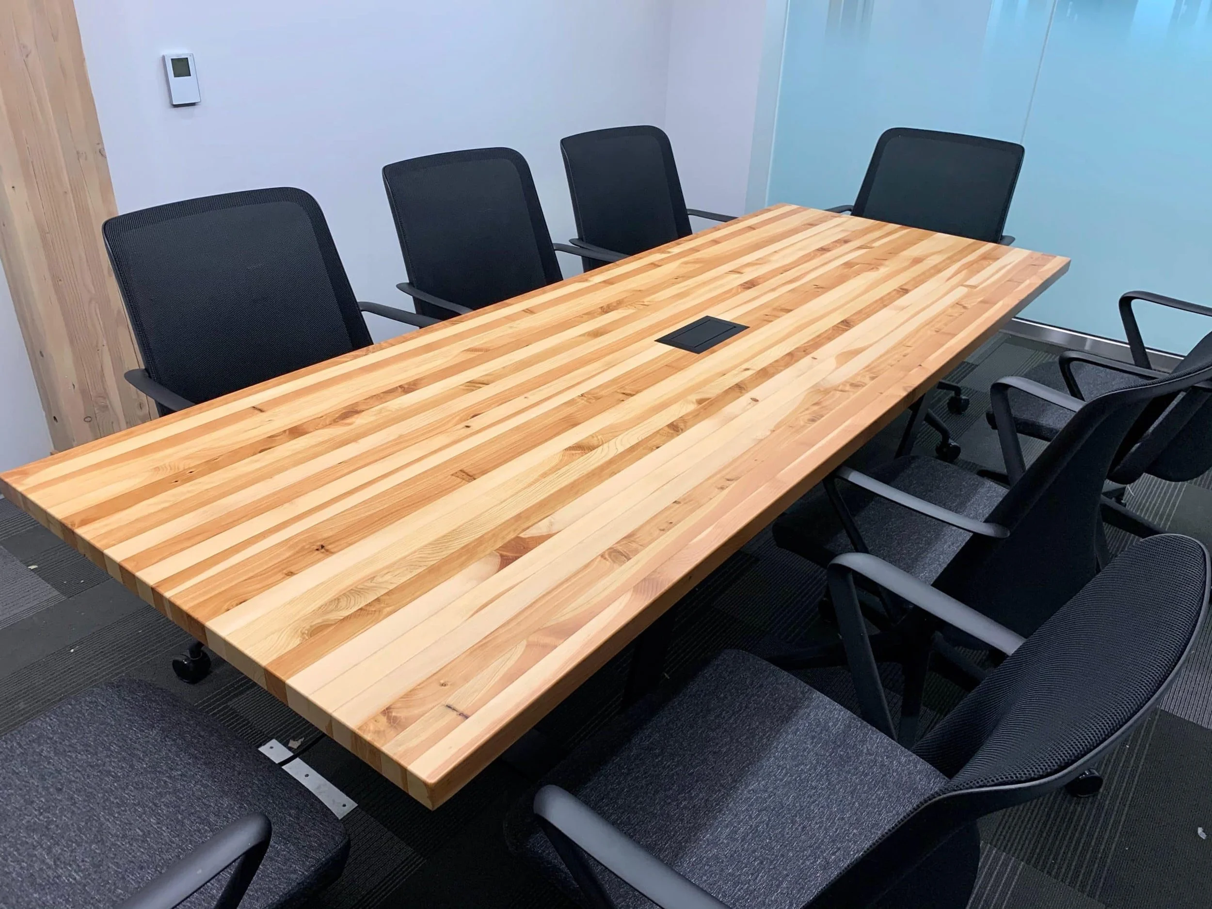 Wooden conference table surrounded by six black office chairs in a modern meeting room.