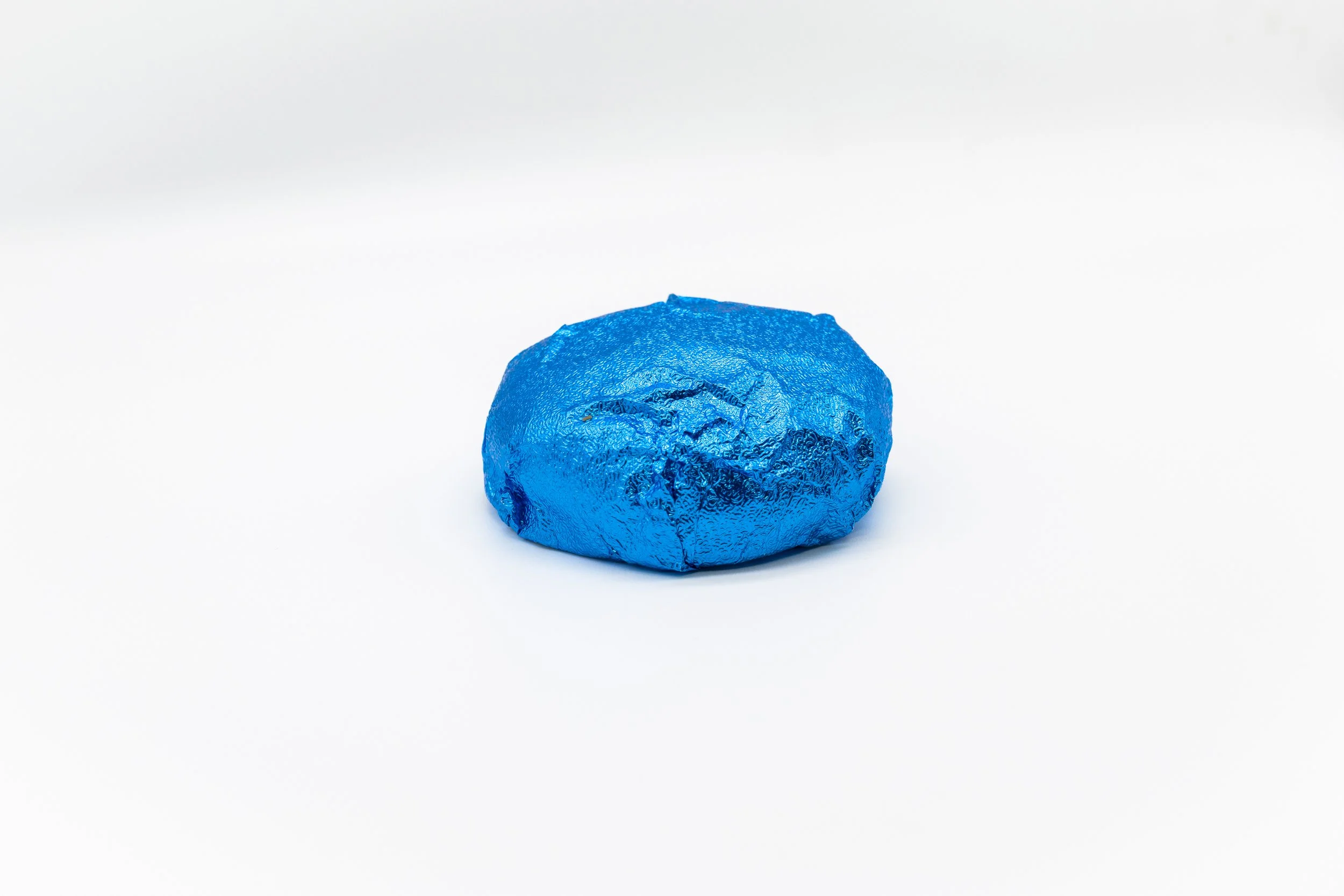 A small, crumpled piece of blue foil wrapping on a white background.