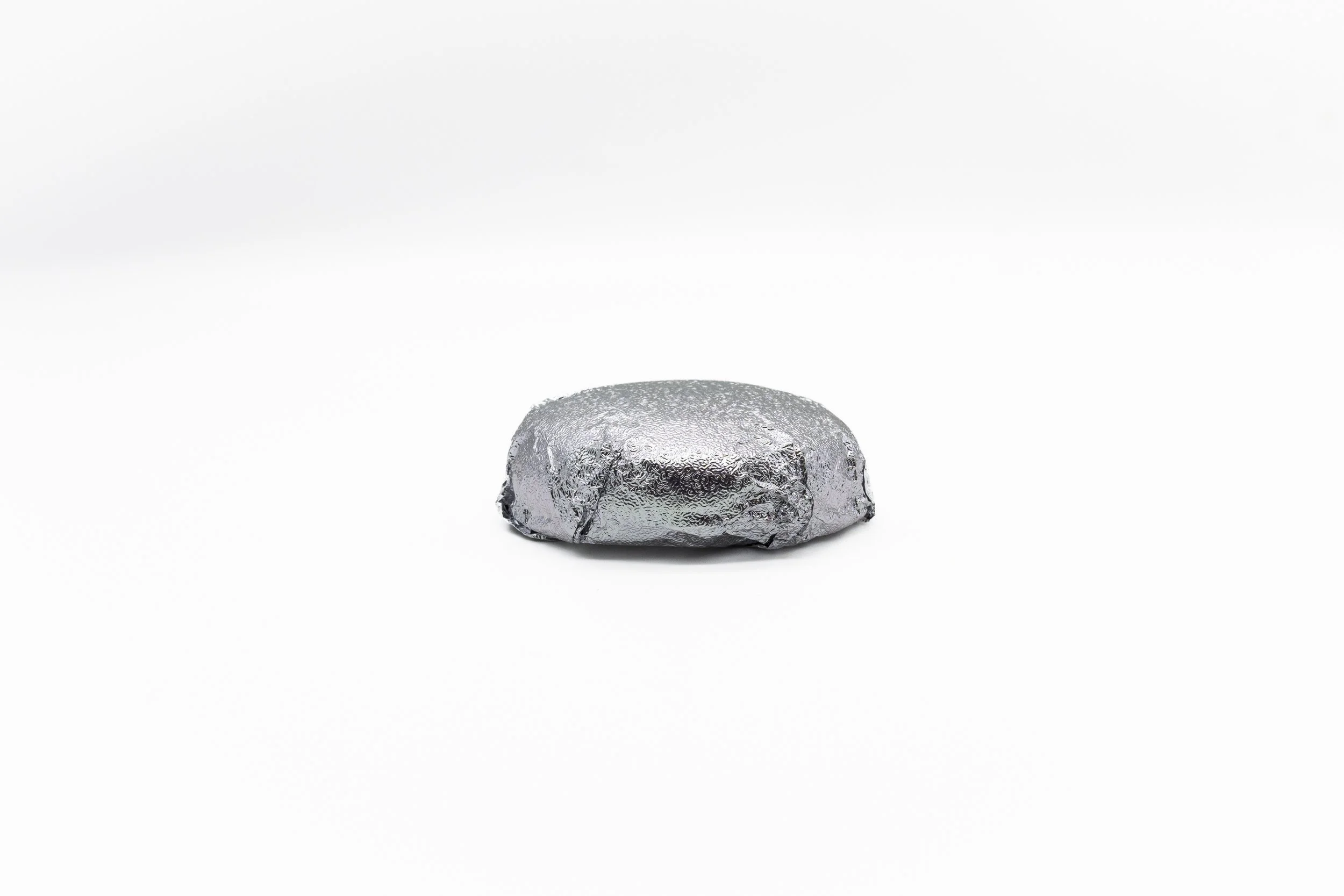 A small, rounded object wrapped in shiny silver foil on a white background.
