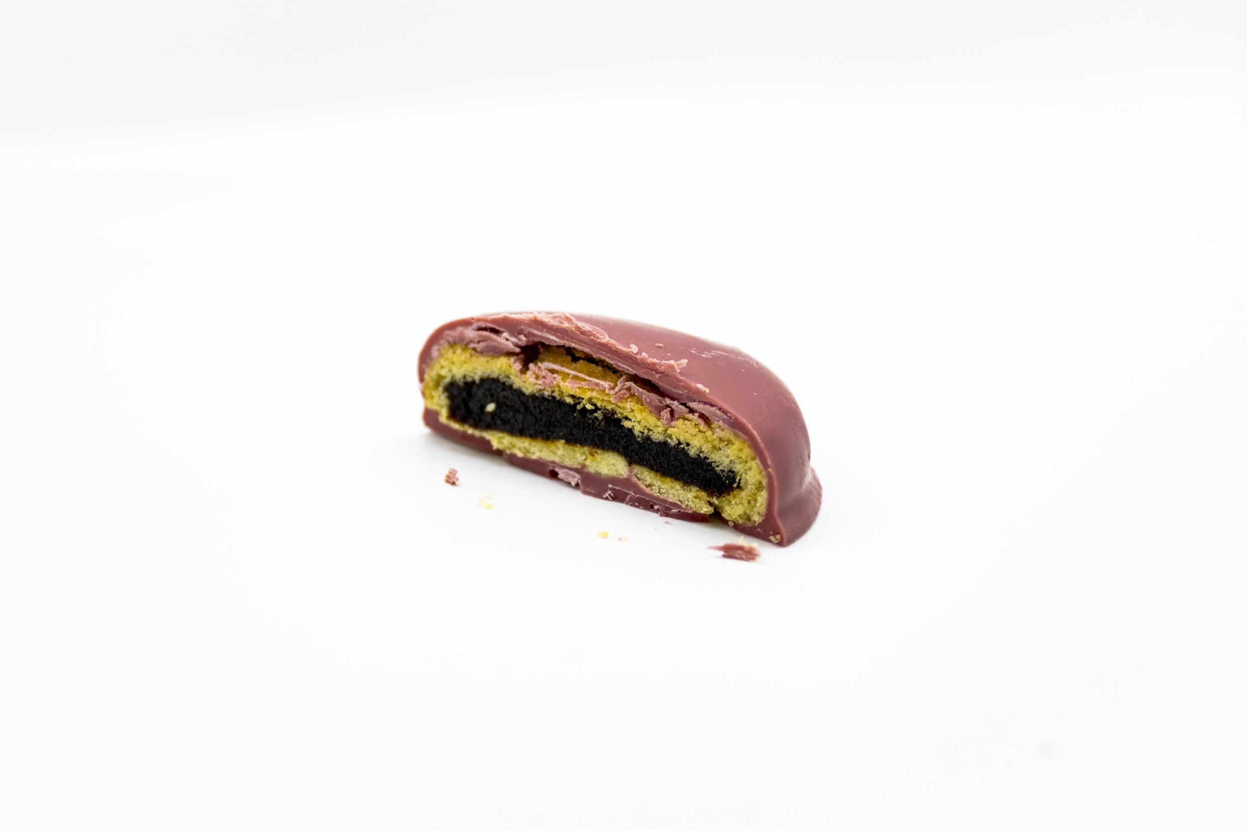 A partially eaten chocolate-covered cookie with yellow cake layers and a dark filling inside, placed on a white background.