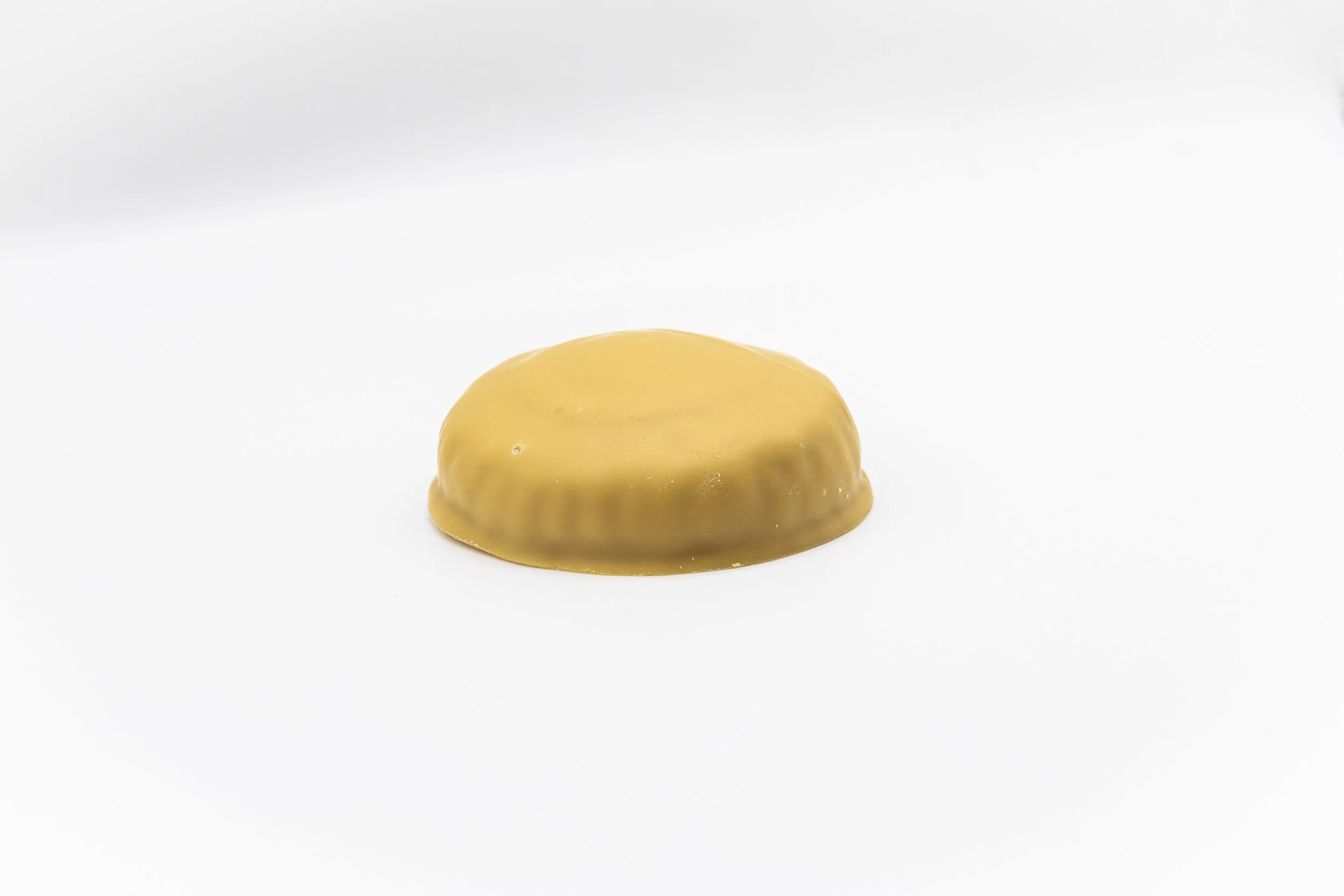 Single yellow chocolate-covered caramel candy on a white background
