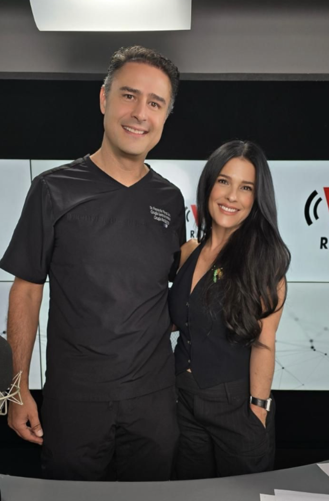 Dos personas posando en un estudio de radio o grabación, fondo con logotipo de radio, ambos sonriendo.