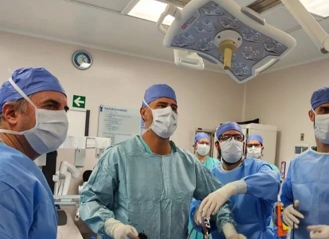 Grupo de cirujanos en una sala de operaciones preparados para una cirugía, con batas, máscaras y guantes.