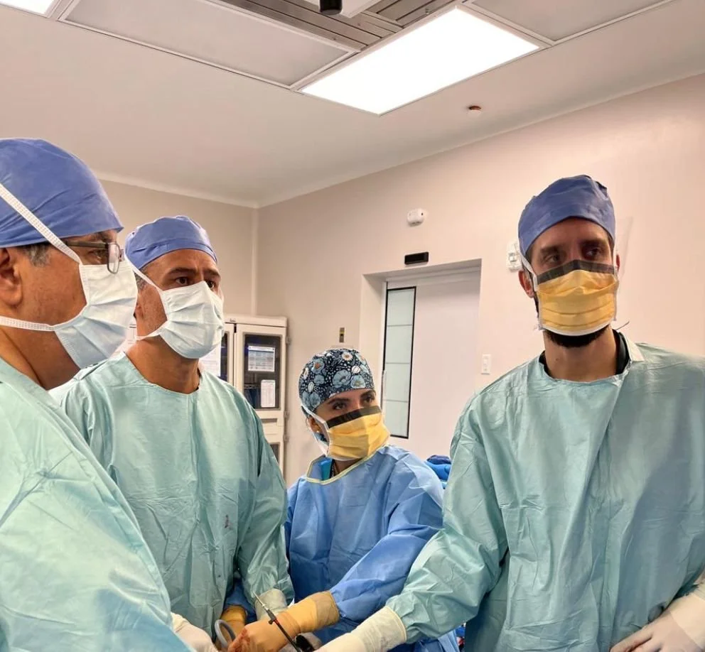 Cuatro profesionales médicos en un quirófano durante una cirugía, usando batas, gorros y mascarillas.
