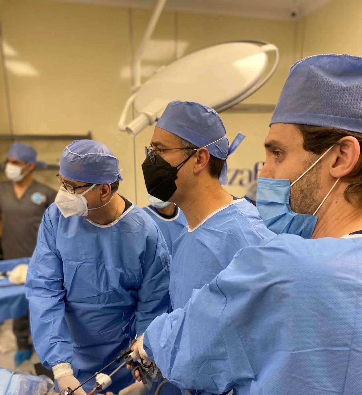Grupo de cirujanos en un quirófano durante una operación, todo con batas, gorros y mascarillas azules.