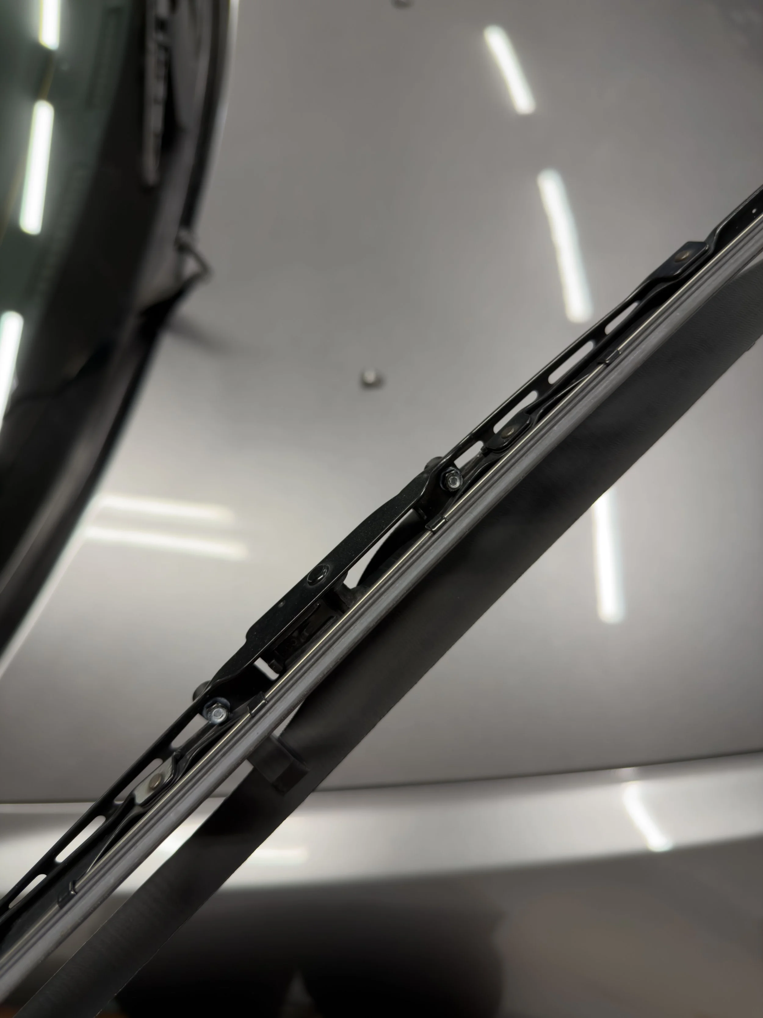 	
Close-up of a vehicle's windshield wiper mechanism and metal frame with the APX Wiper Wing installed.