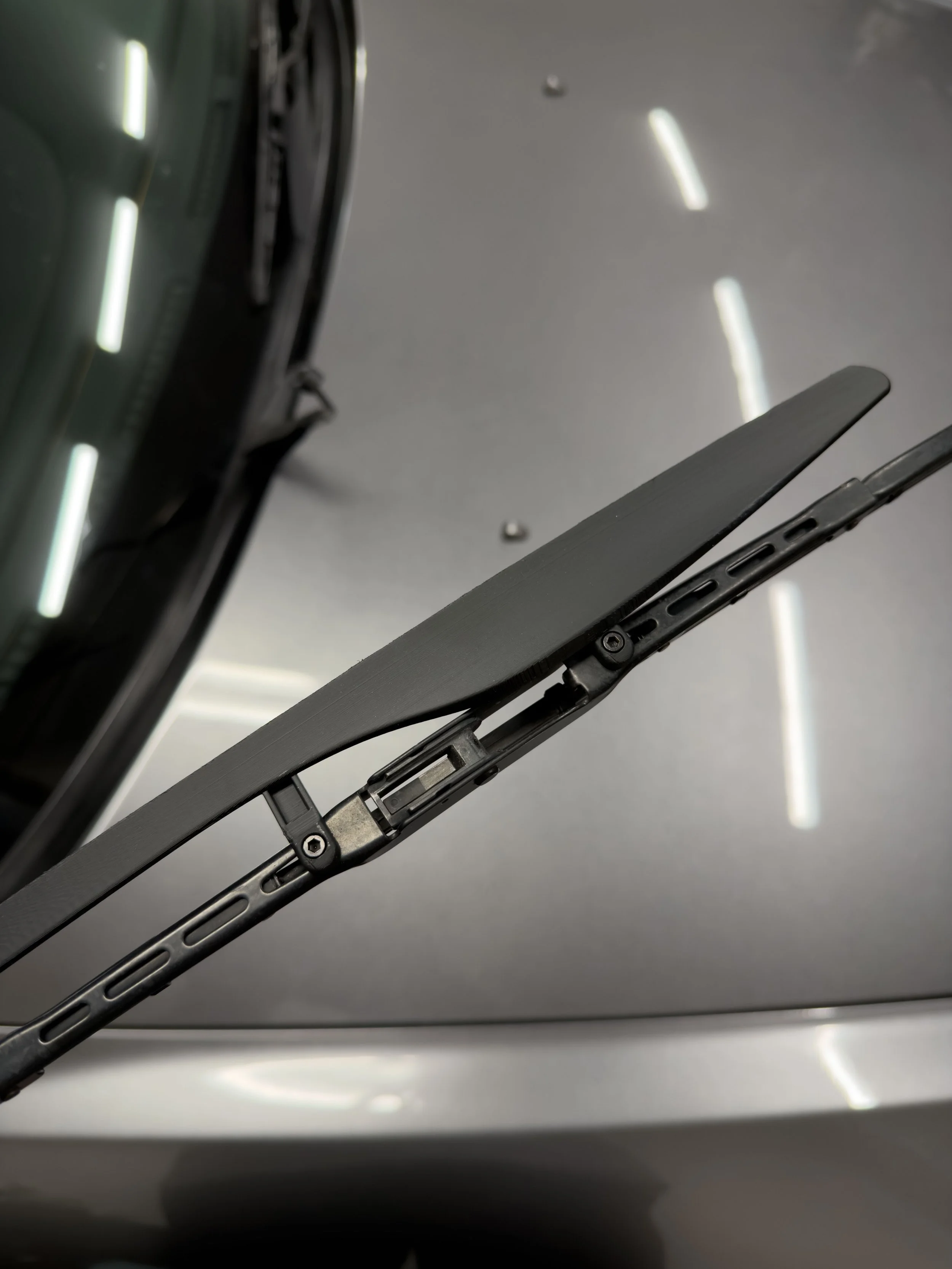 Close-up of an open laptop hinge showing the laptop's screen and keyboard, with a gray background and ceiling lights reflecting on the surface.