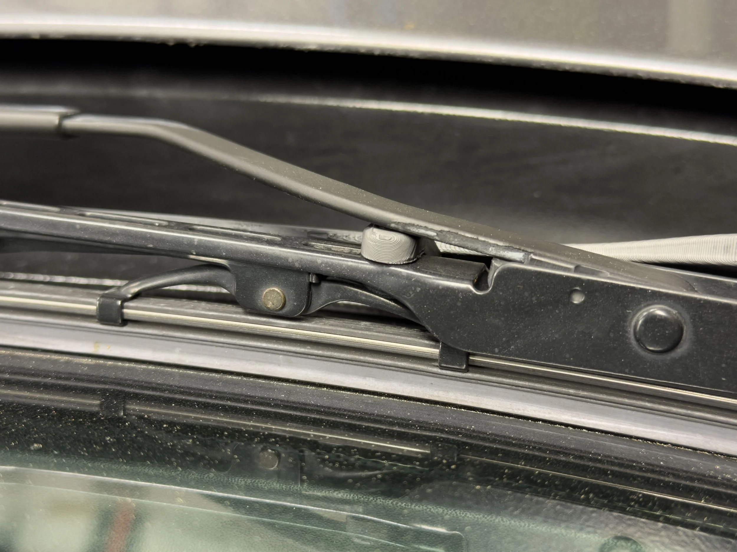 Close-up of a vehicle's windshield wiper mechanism and metal frame.