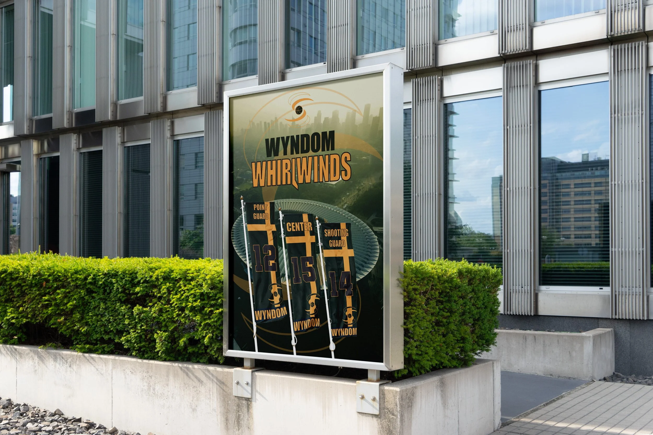 Outdoor billboard advertising WYNDOM WHIRLWINS with miniature football goalposts numbered 12, 15, and 14, set against a modern glass building and a well-kept green shrub background.