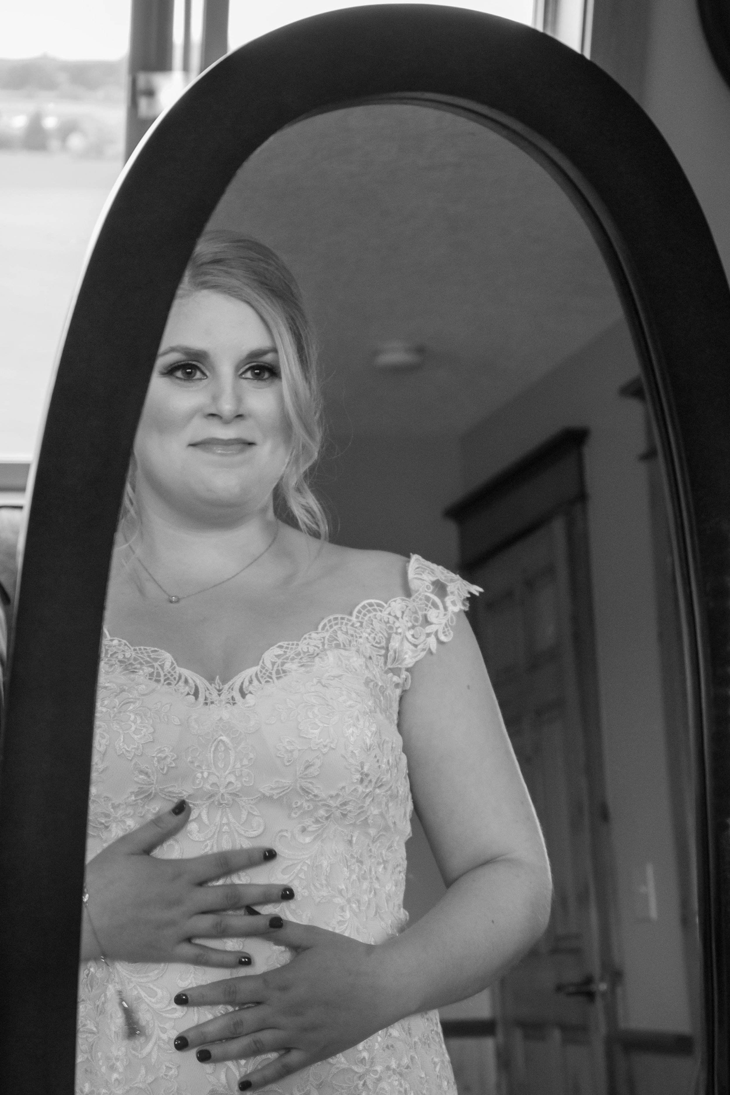 A woman in a lace dress looking into an oval mirror, with her hand on her chest, black and white photo.