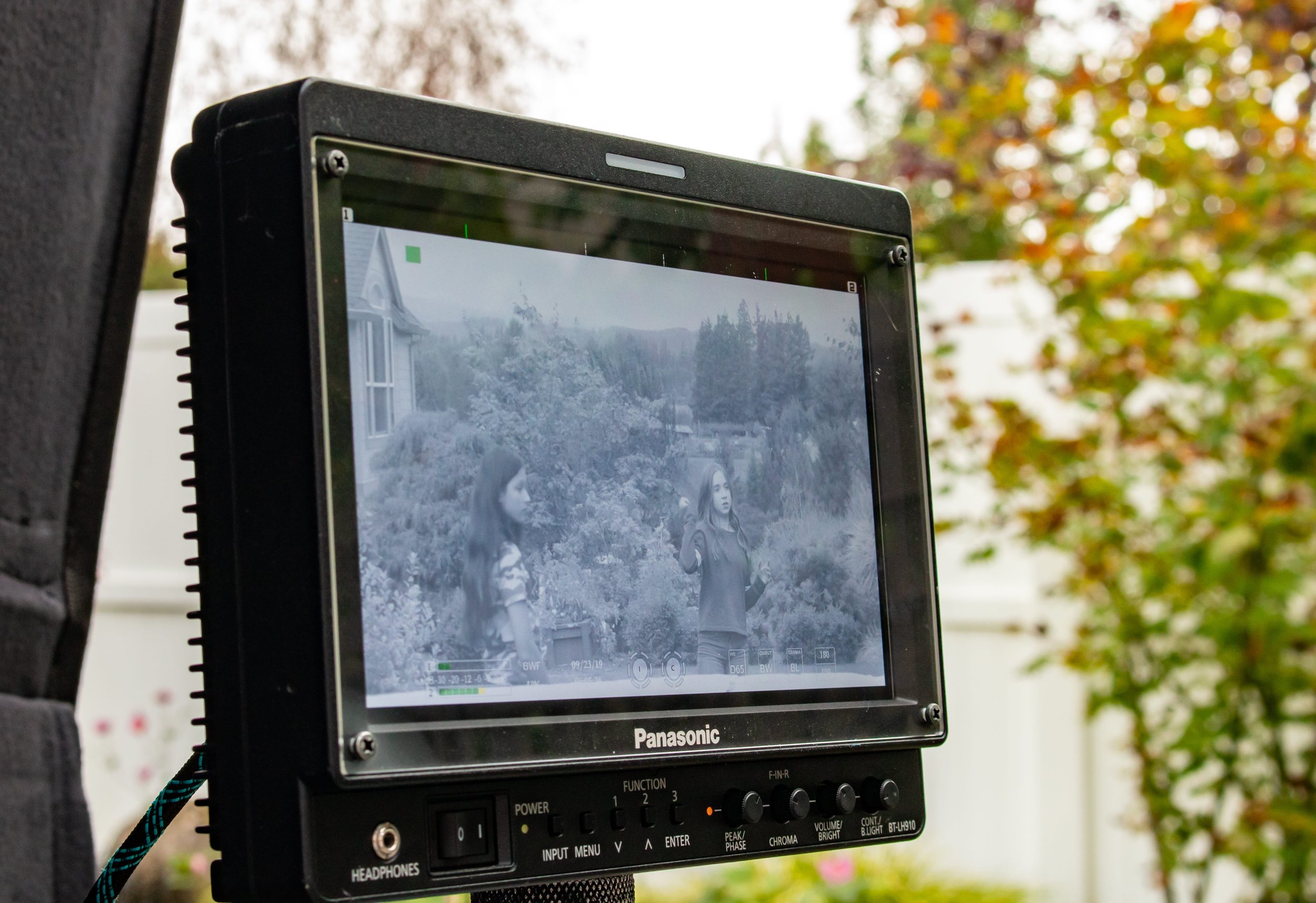 Movie director's monitor showing a scene of two women talking outdoors, with a house and trees in the background.