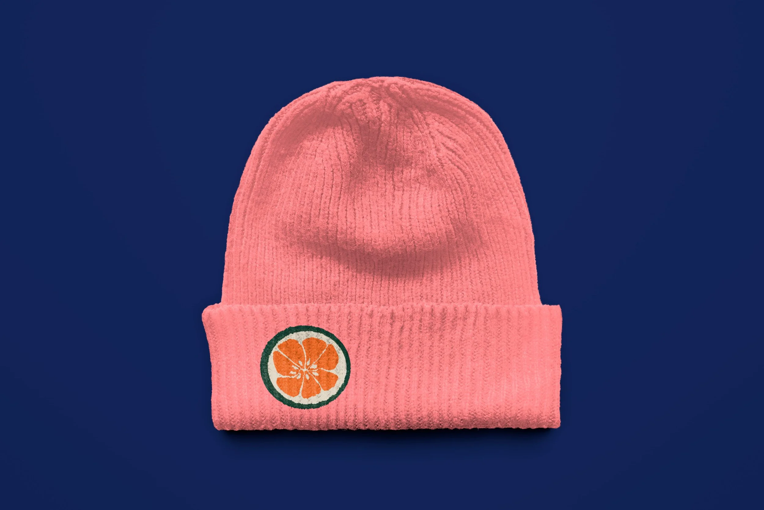 Pink knit beanie with orange slice logo on a dark blue background.